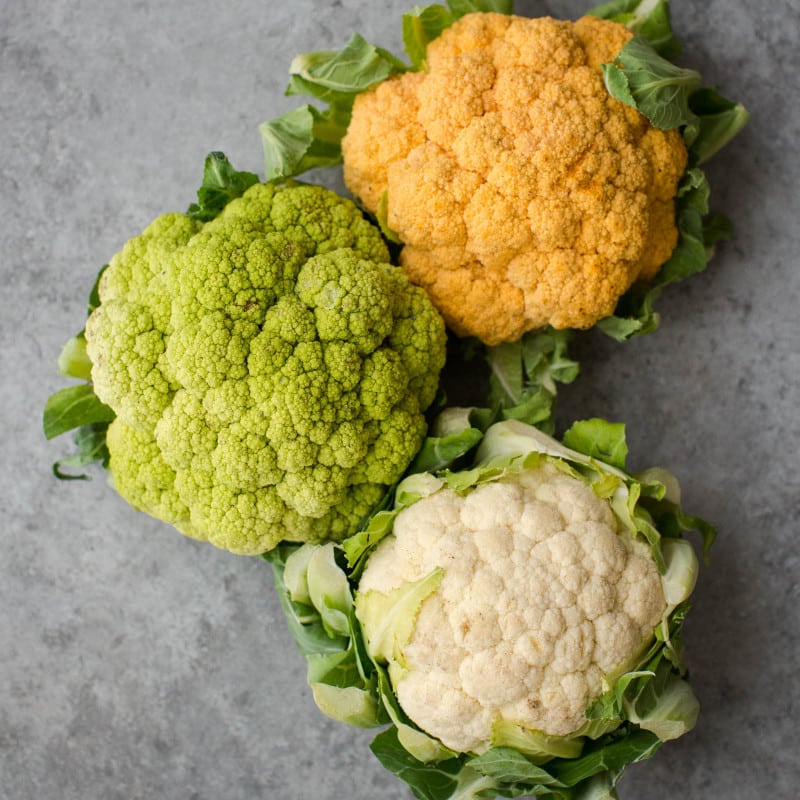 Overhead shot of orange, green, and white cauliflower heads.