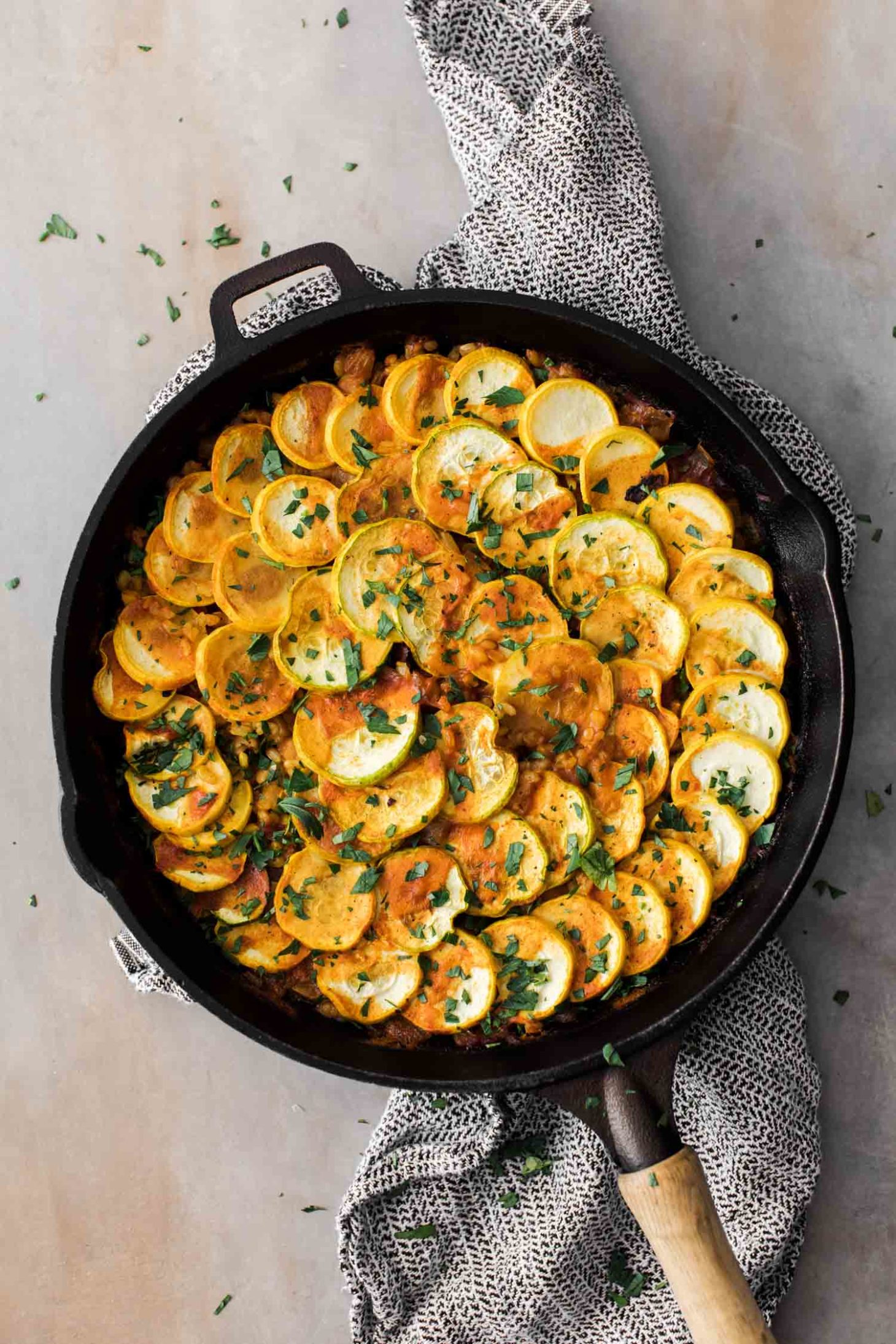 Overhead shot of a cast iron skillet with paella layered with summer squash