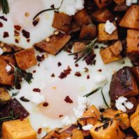 Close-up, overhead photo of roasted sweet potatoes with baked eggs nestled in among the sweet potatoes.