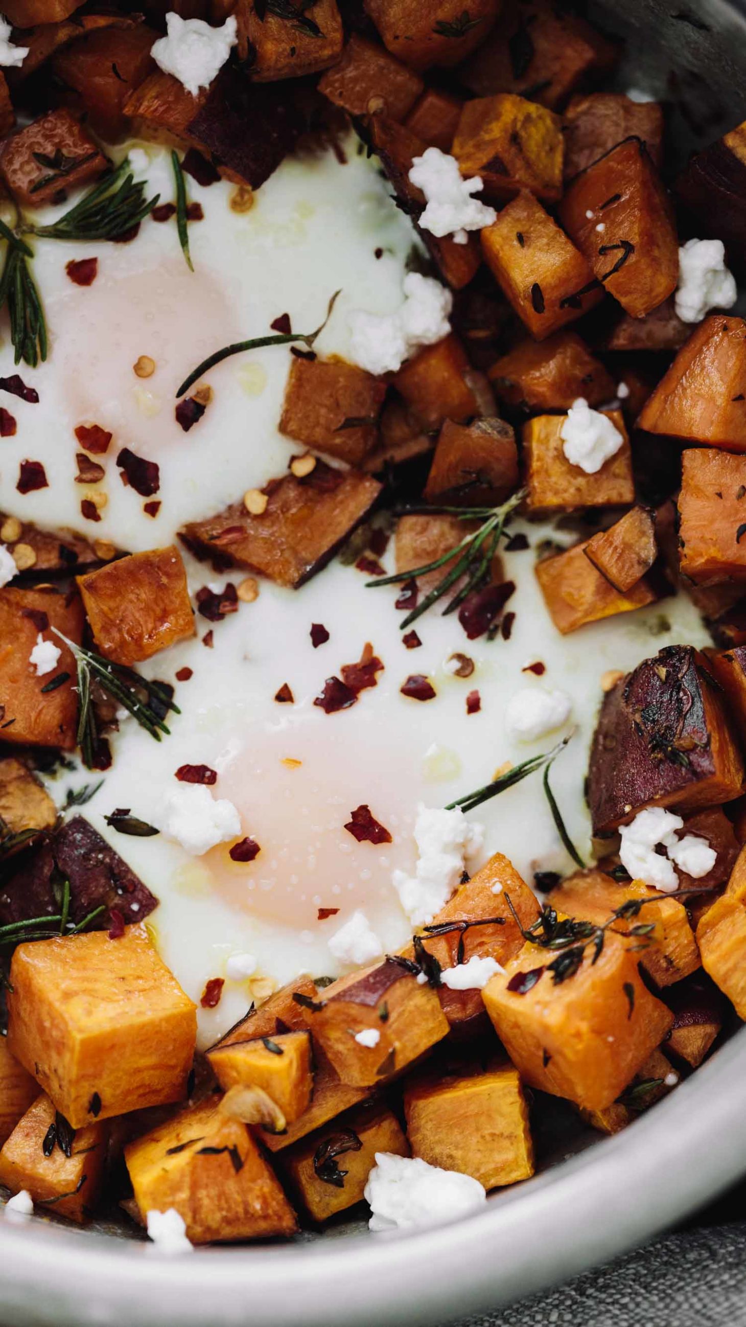 Close-up, overhead photo of roasted sweet potatoes with baked eggs nestled in among the sweet potatoes.