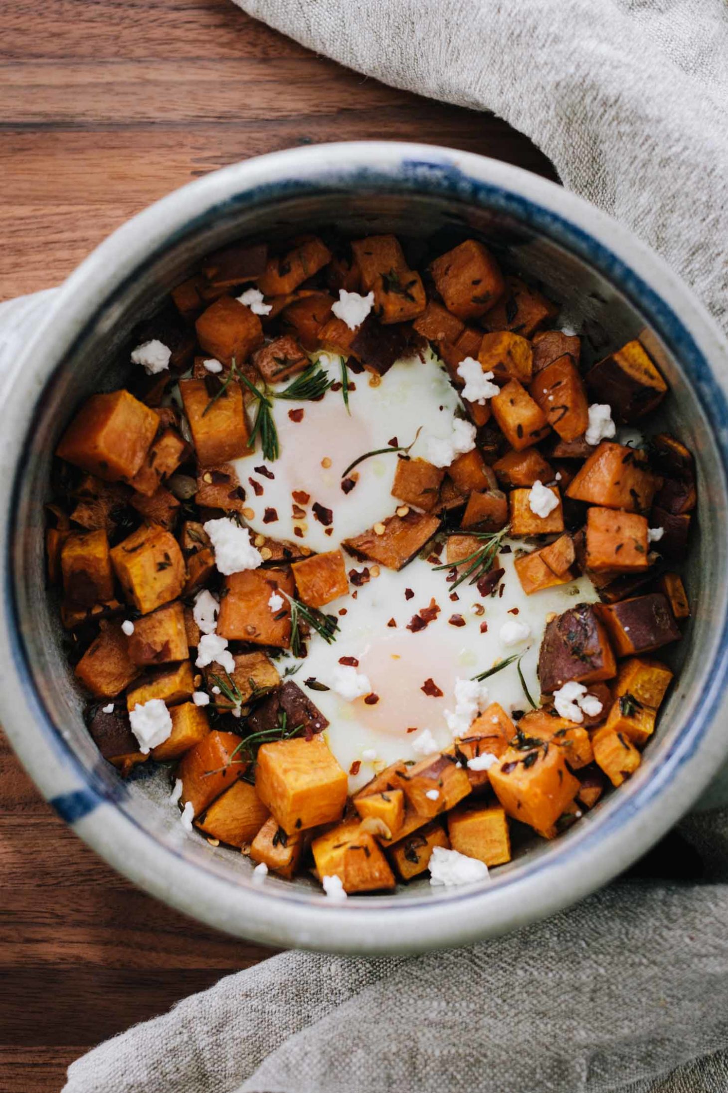 Overhead photo of roasted sweet potatoes and baked eggs, topped with rosemary and goat cheese.