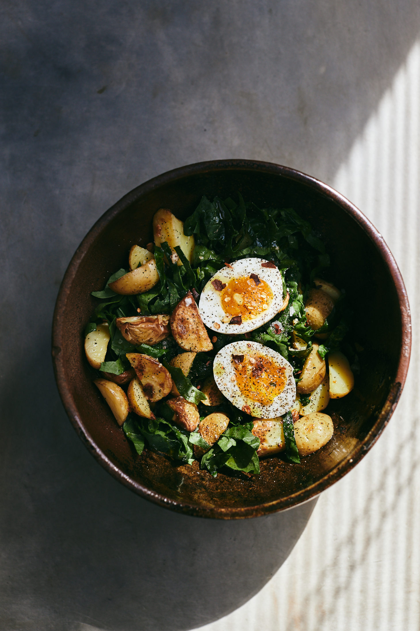 Overhead photograph of a spinach salad topped with roasted potato wedges and soft-boiled eggs.
