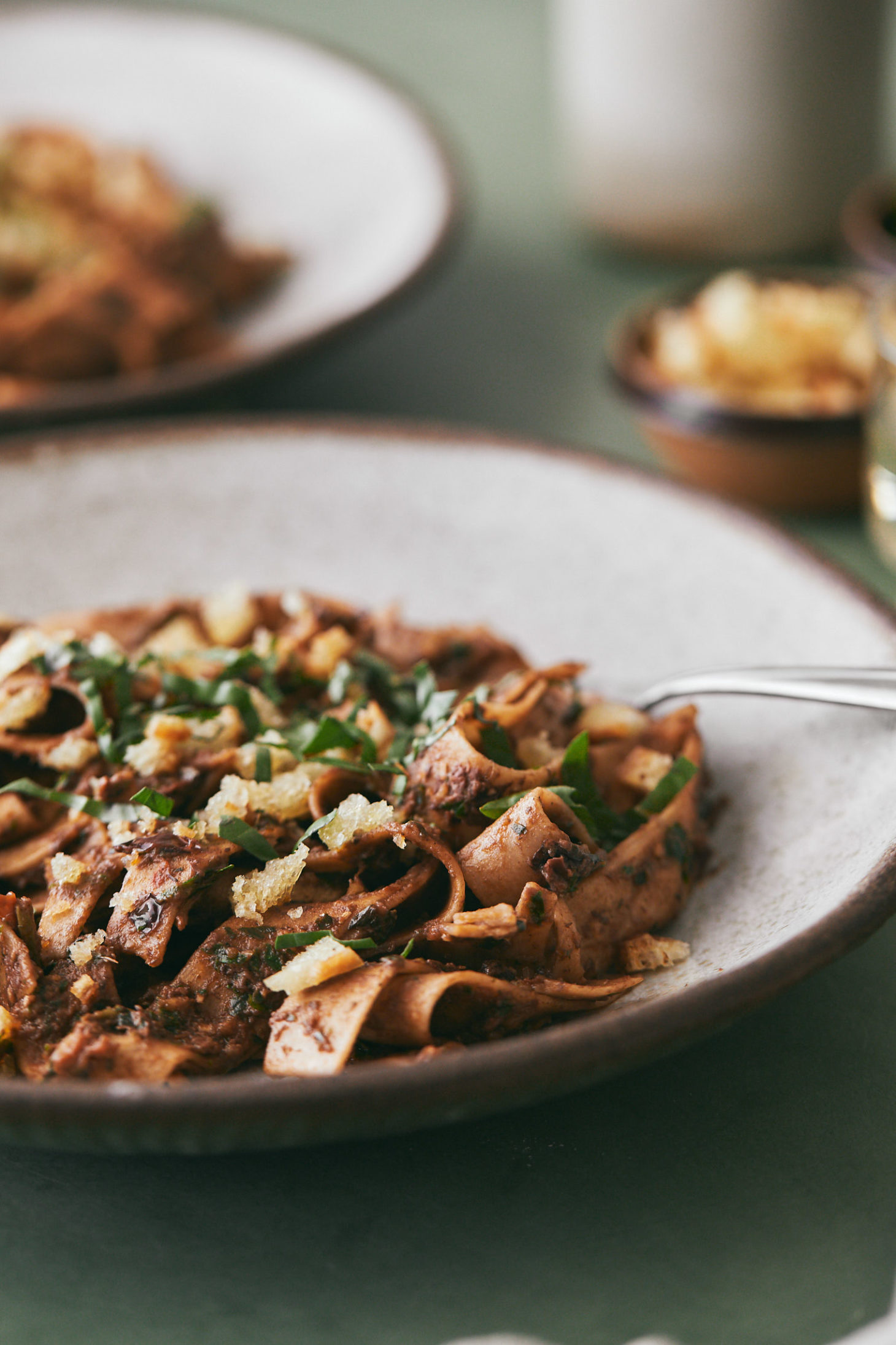 Close-up, side angle photograph of long pasta in an olive sauce and topped with basil.