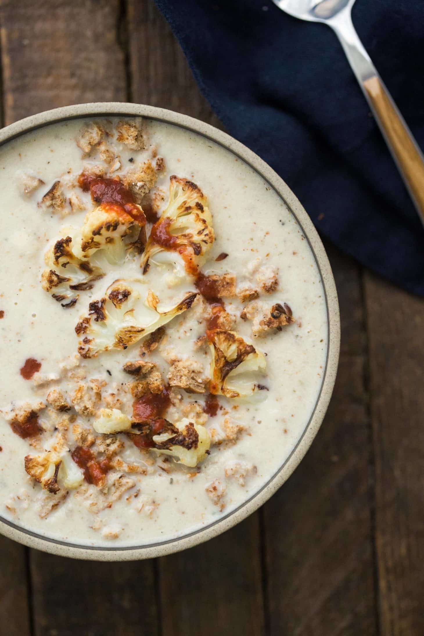 Close-up, overhead photograph of cauliflower soup topped with pieces of roasted cauliflower, breadcrumbs, and hot sauce. 
