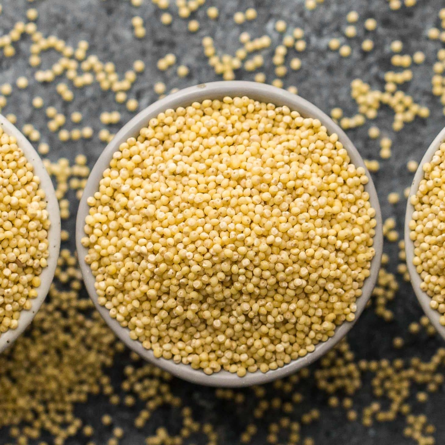side-angle photo of cooked millet being spooned out of a stainless steel pot-ready to use in millet recipes