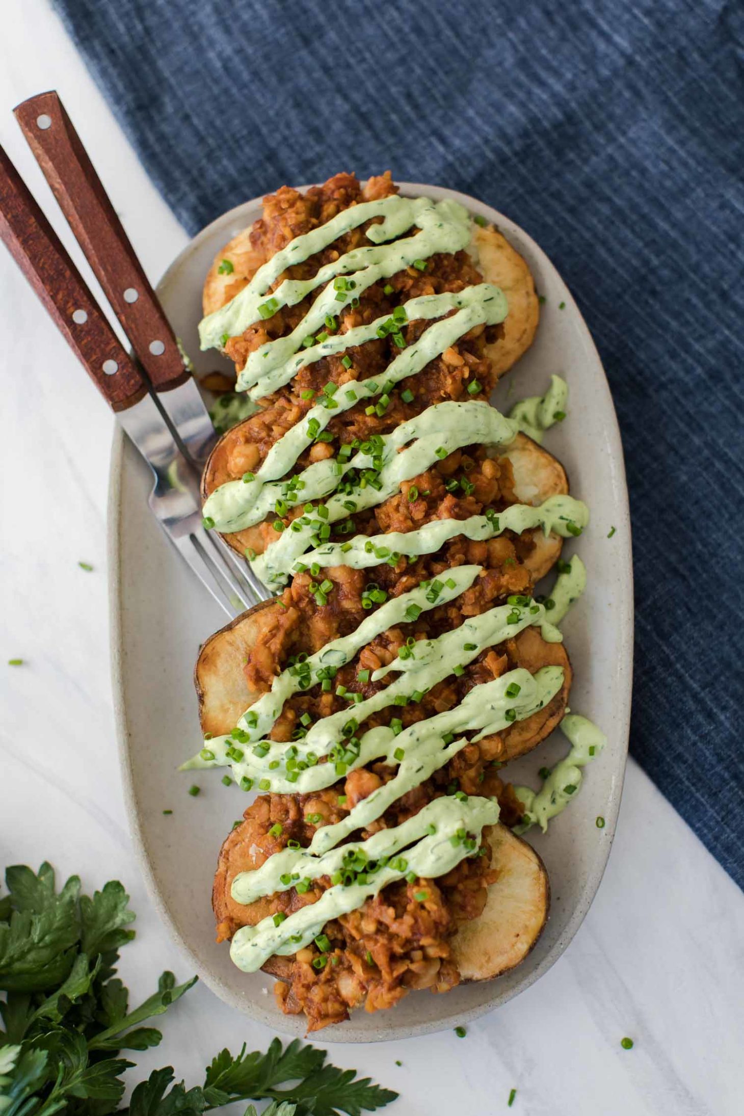 Overhead shot of baked potatoes covered with bbq chickpeas and green avocado ranch dressing.