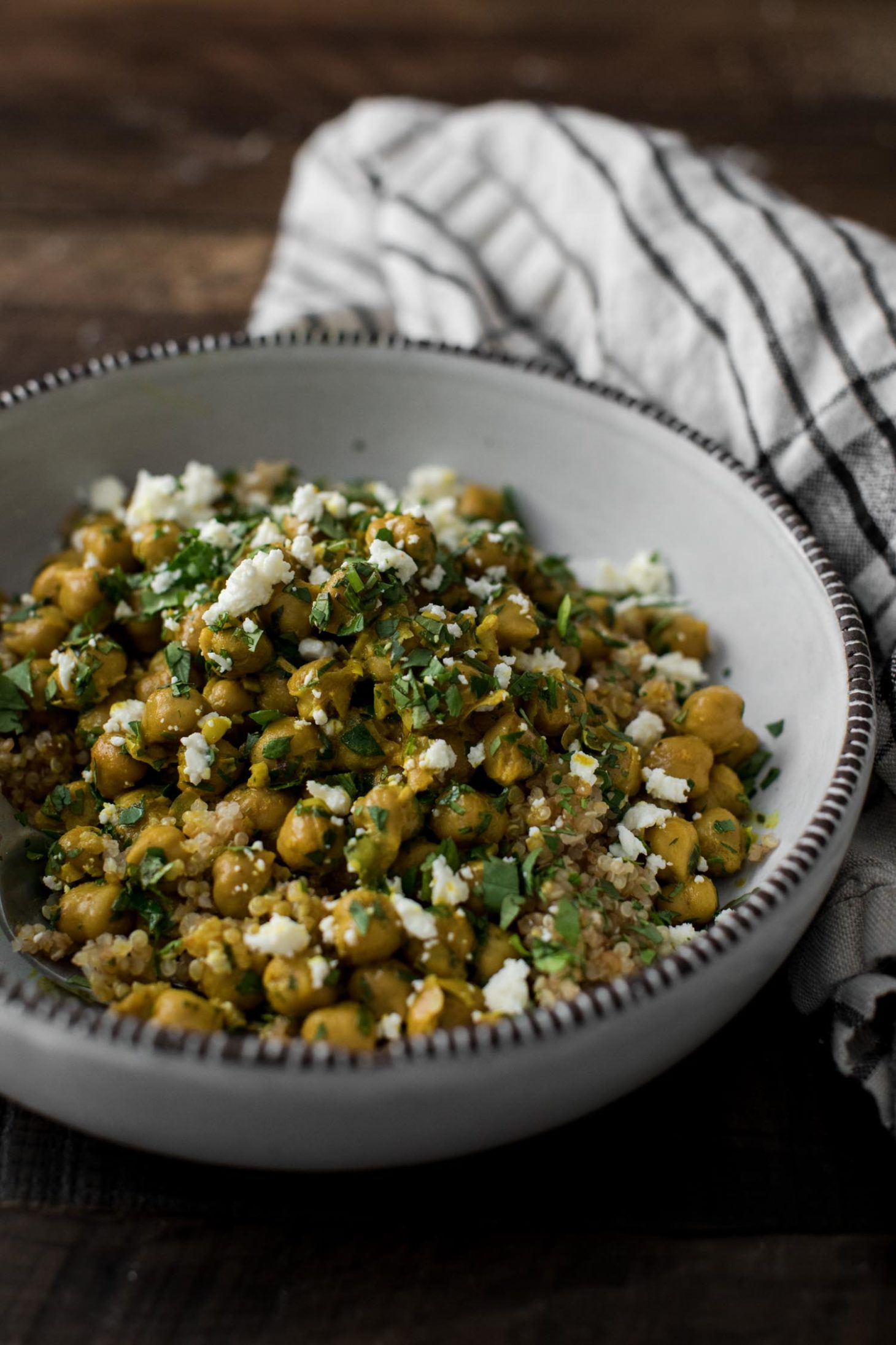 Side-angle shot of a light bowl containing curried chickpeas topped with feta