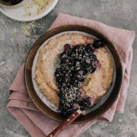 Overhead shot of bluberry spelt porridge topped with hemp seeds and cream.