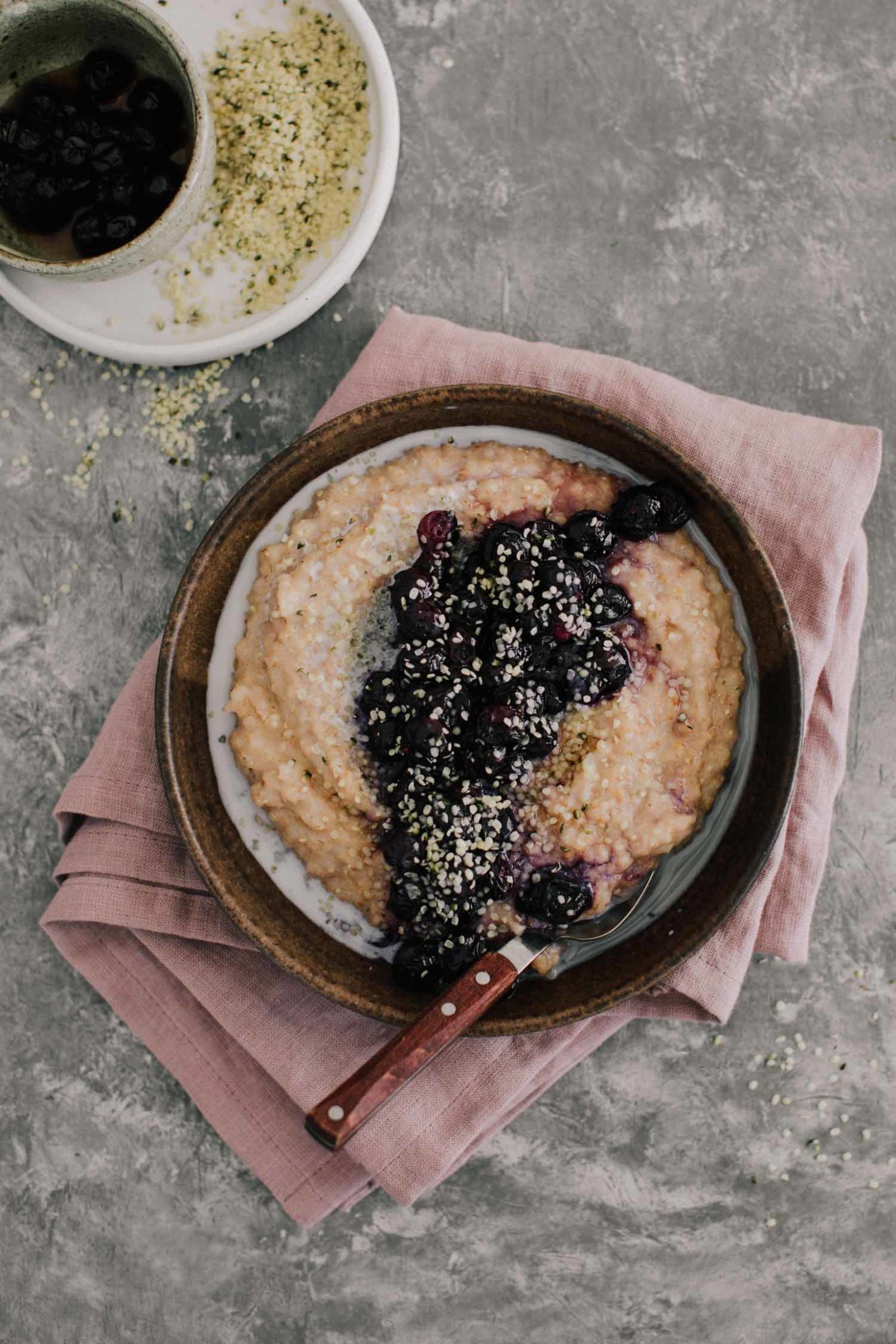 Overhead shot of bluberry spelt porridge topped with hemp seeds and cream.