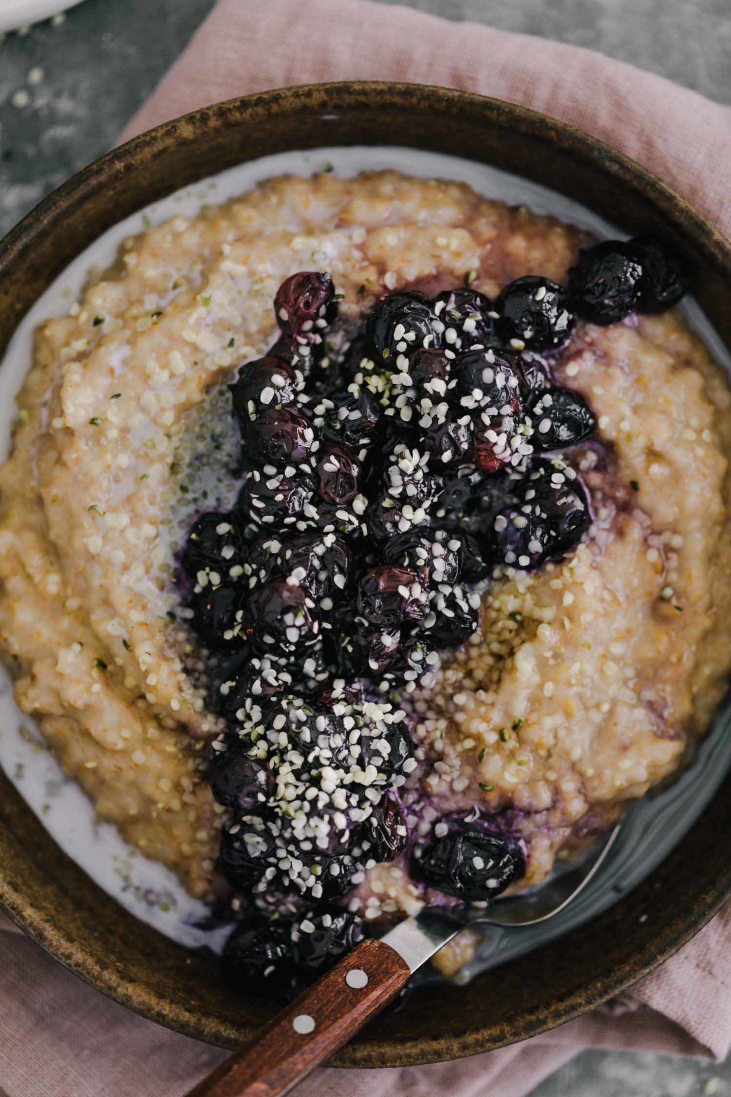 Overhead shot of cracked spelt porridge topped with roasted blueberries and hemp seeds