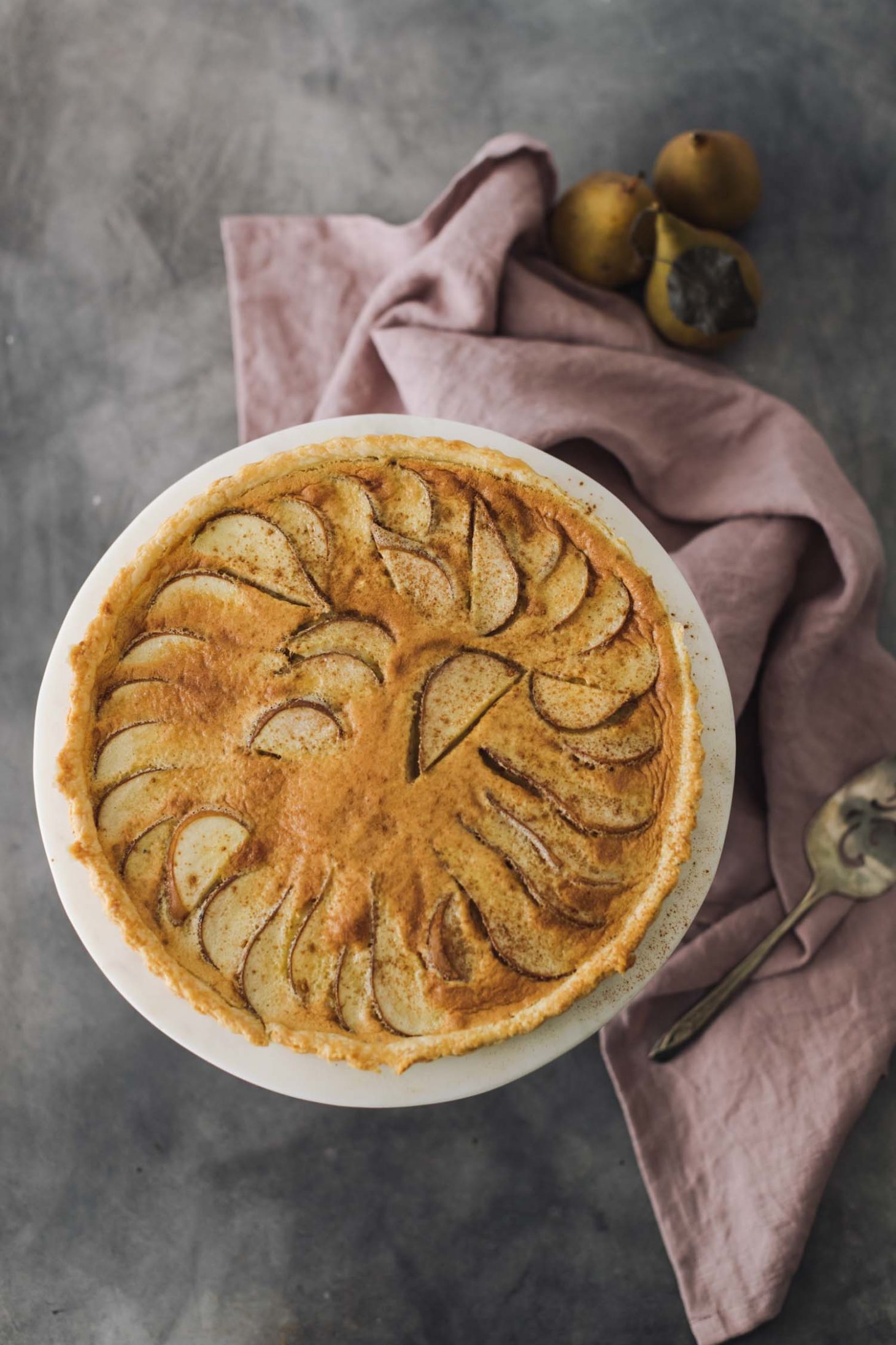 Overhead shot of an 11" tart filled with pears, custard filling, and a sprinkle of cinnamon