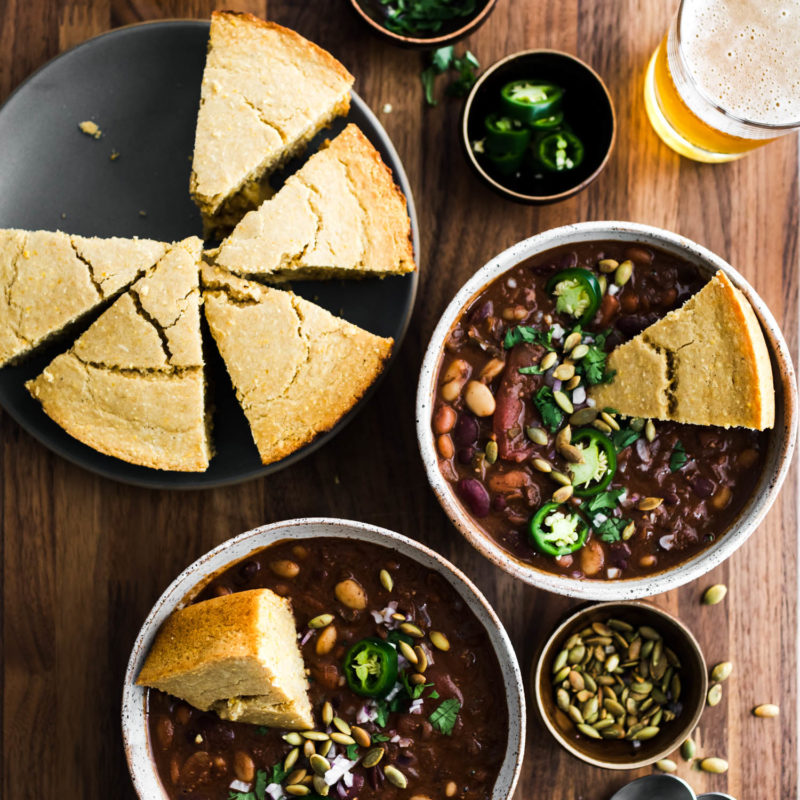 Overhead shot of two bowls of vegan chili filled with beans and topped with jalapeños and cornbread.