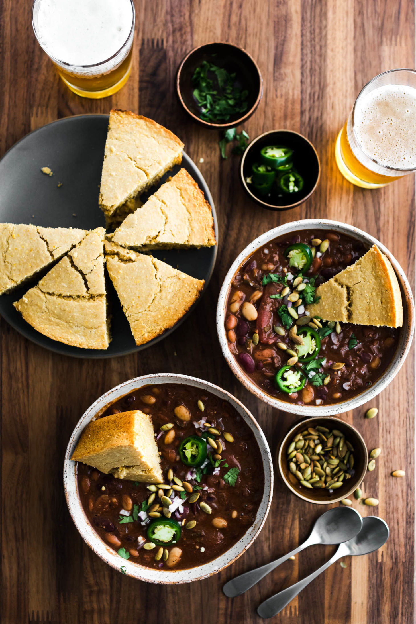 Overhead shot of two bowls of vegan chili filled with beans and topped with jalapeños and cornbread.
