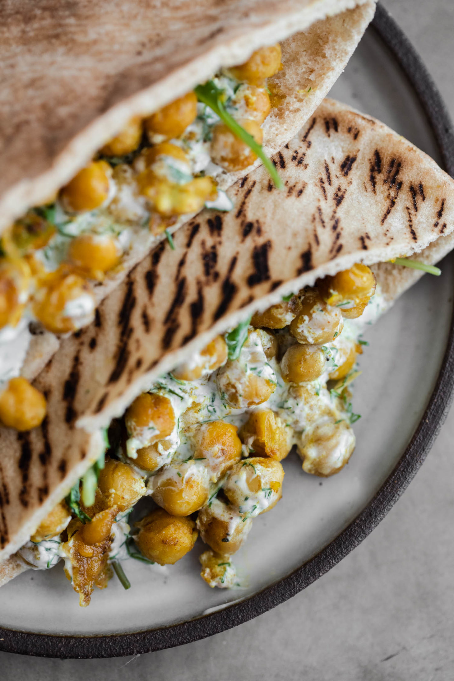 Close-up overhead shot of chickpea curry stuffed in pita with a dill yogurt sauce and arugula.