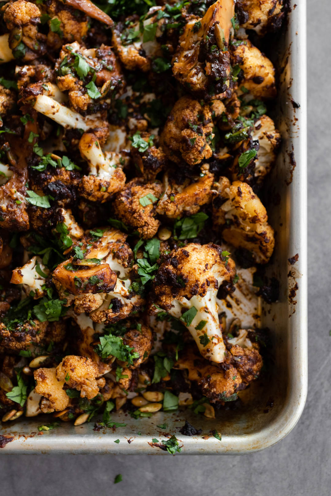 Overhead shot of mole cauliflower on a sheet tray, tossed and roasted with mole sauce.