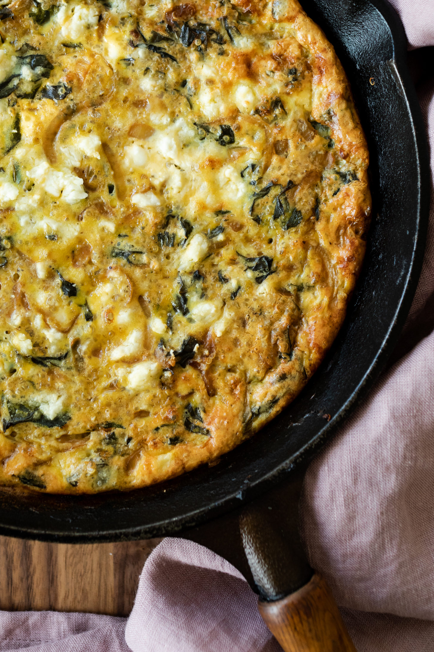 Close-up overhead shot of a chard frittata in a black cast iron pan with a pink napkin.