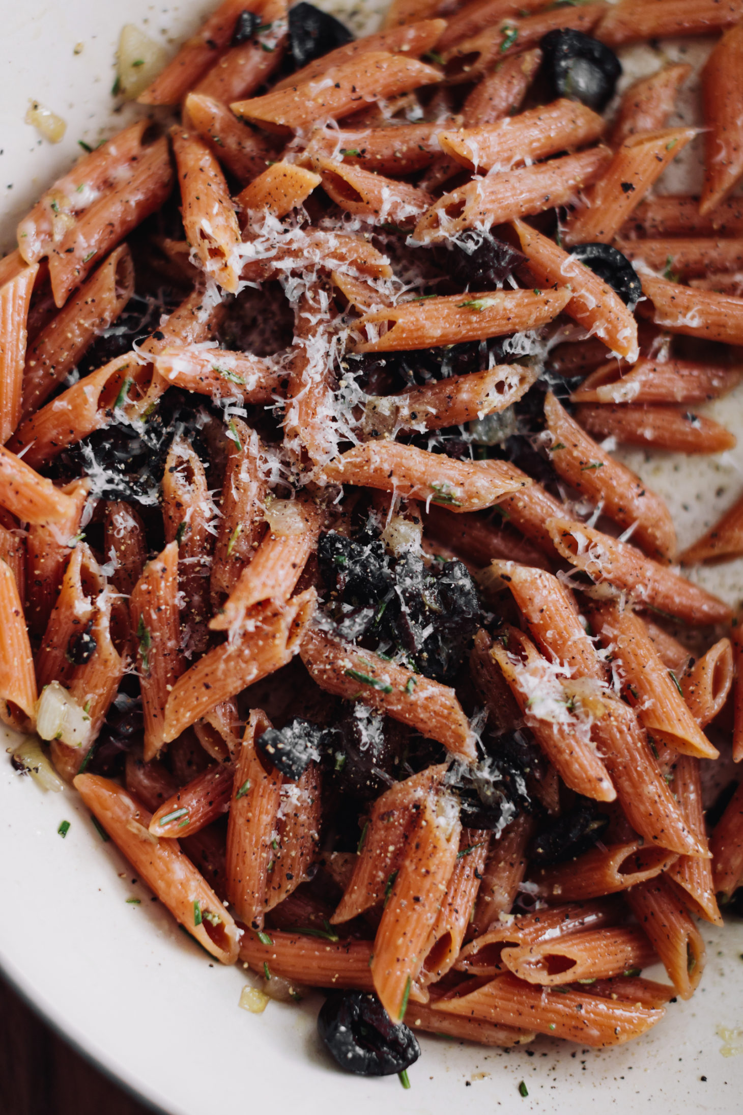 Overhead, close-up photograph of red lentil pasta, cheese, and black olives.