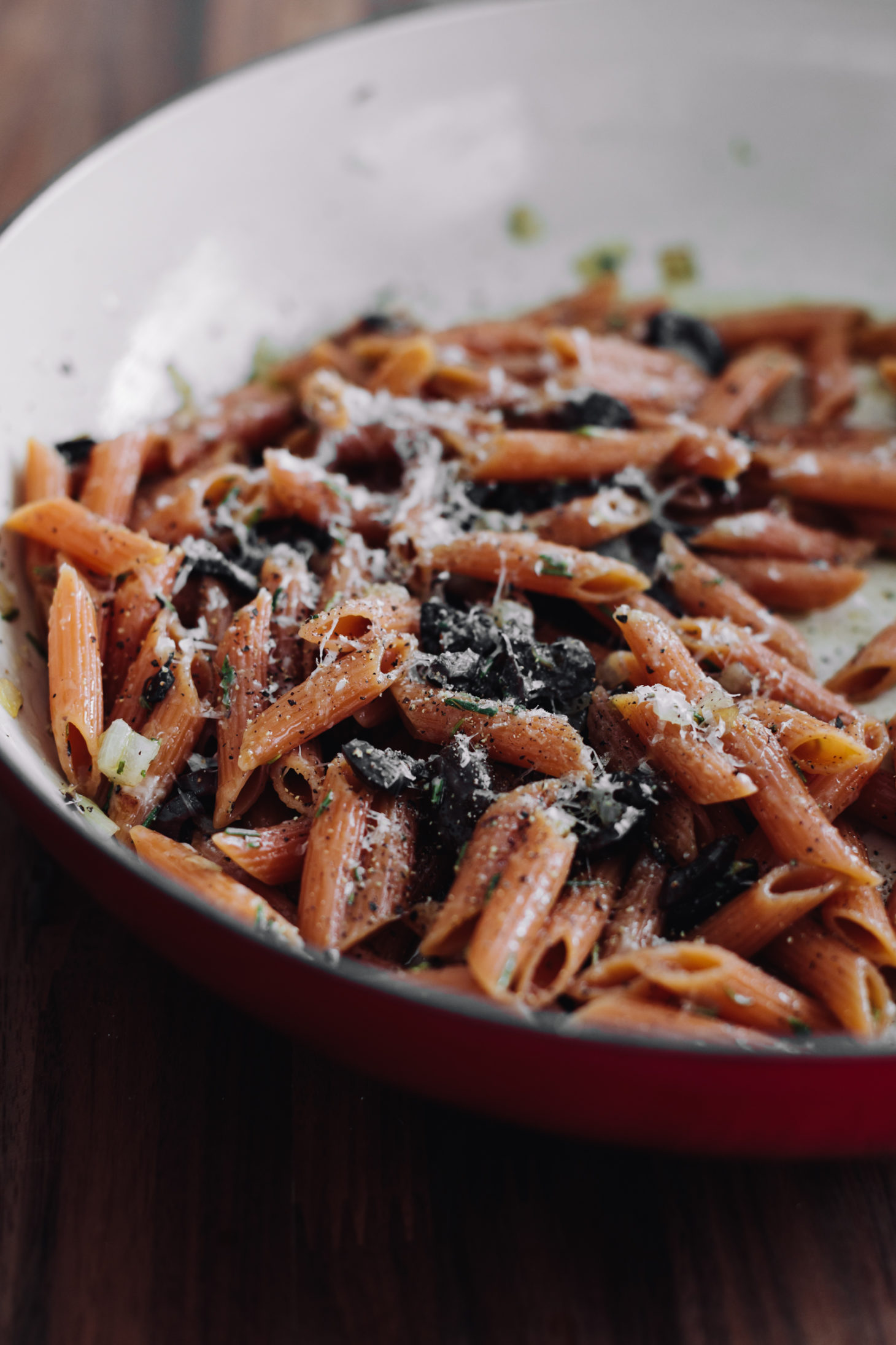 Side-angle photograph of red lentil pasta with black olives and parmesan.