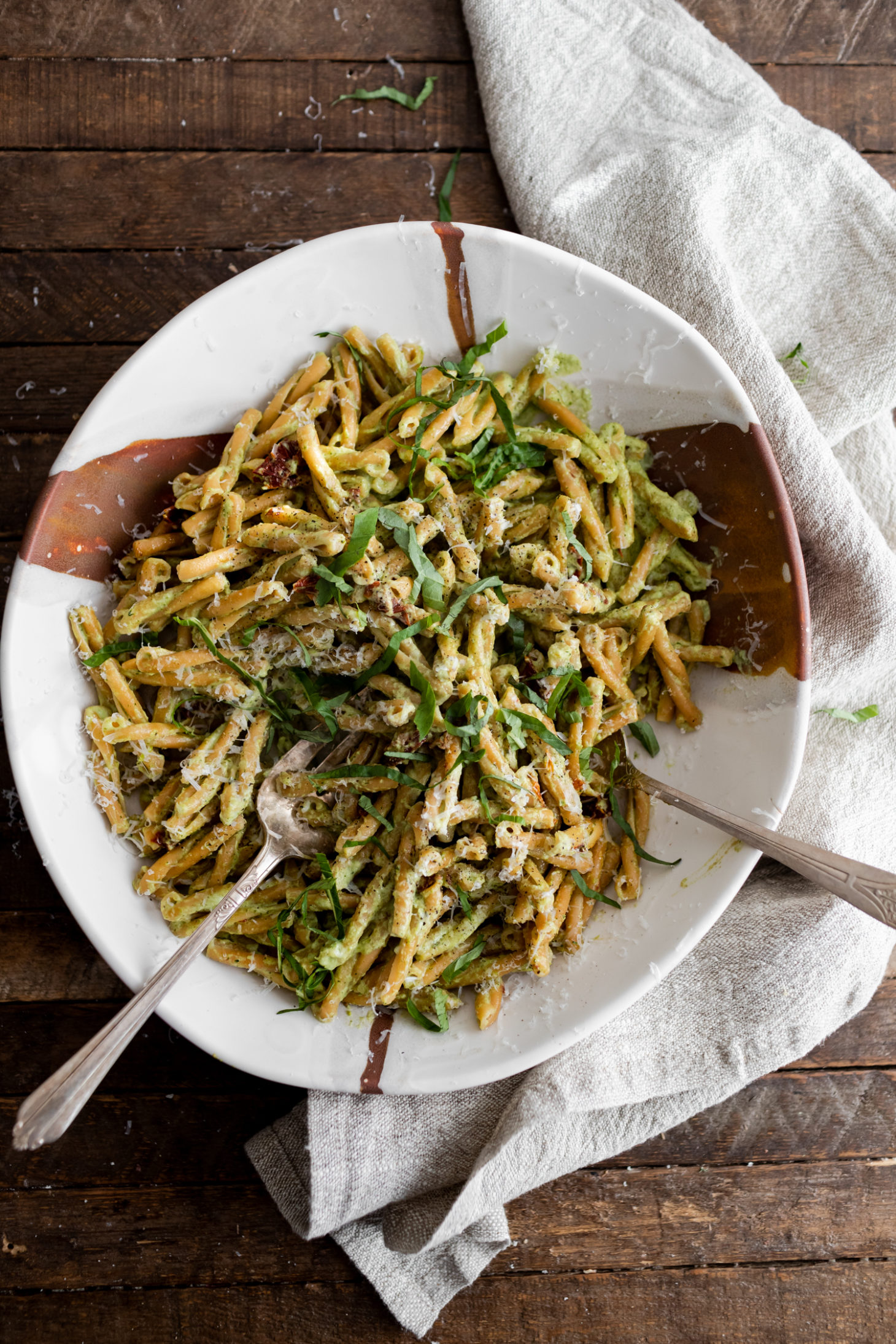 Photograph of a full, large white bowl of pasta tossed with a broccoli pesto. 