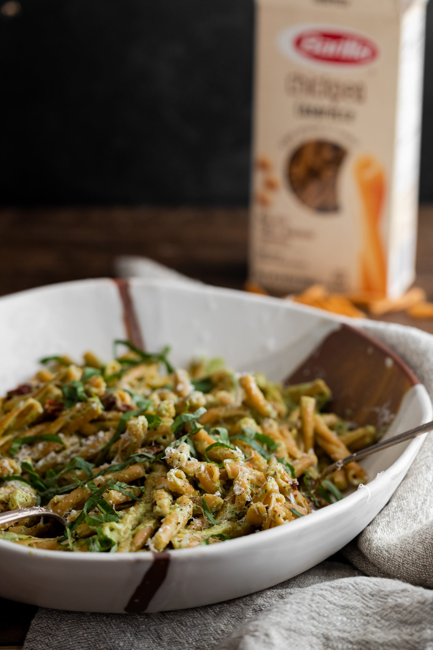 Side angle photograph of a chickpea pasta tossed in a broccoli pesto, served in a large white dish.