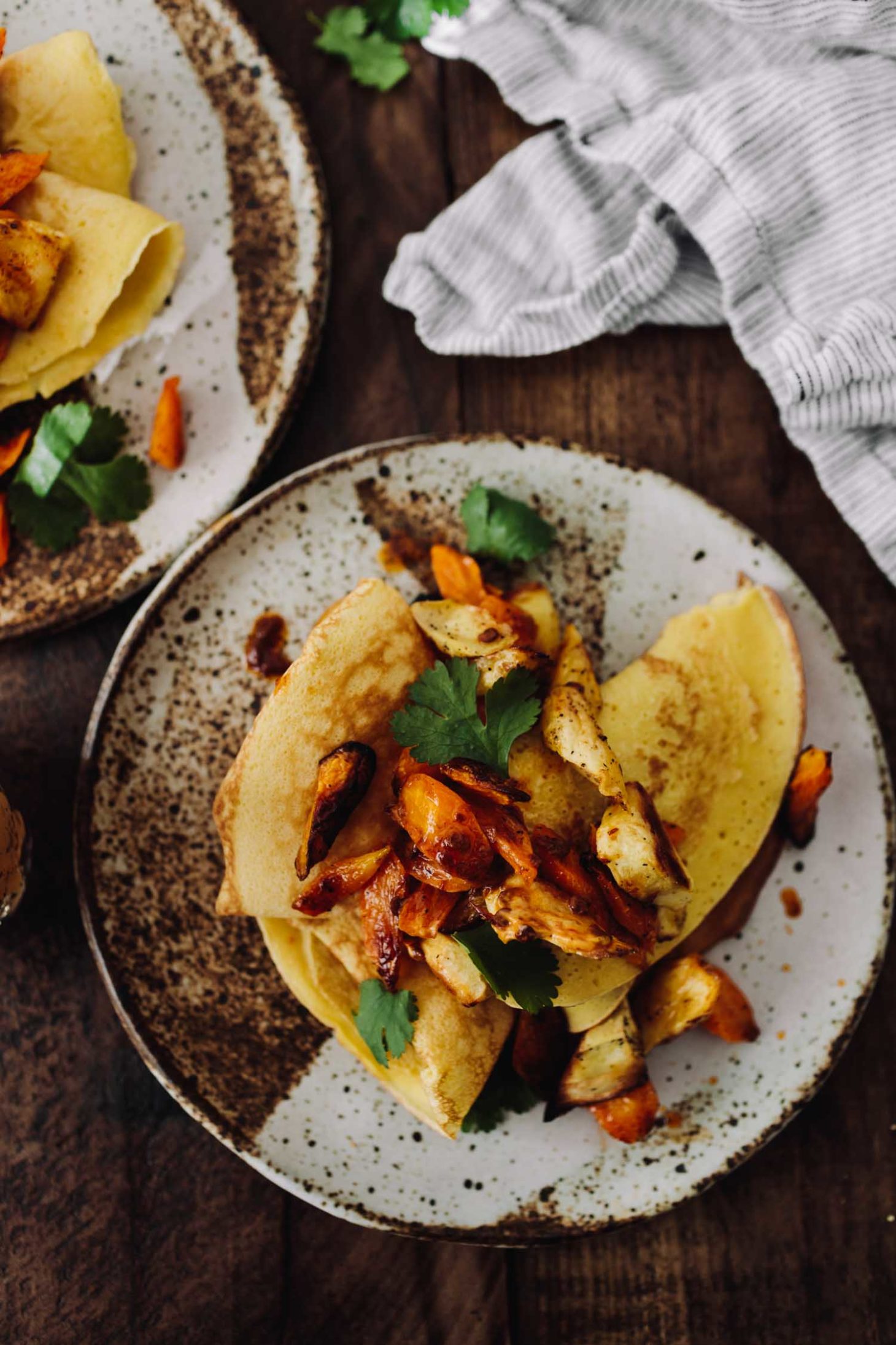 Overhead photo, close-up, of yellow chickpea crepes topped with parsnip and carrot pieces and chipotle compound butter