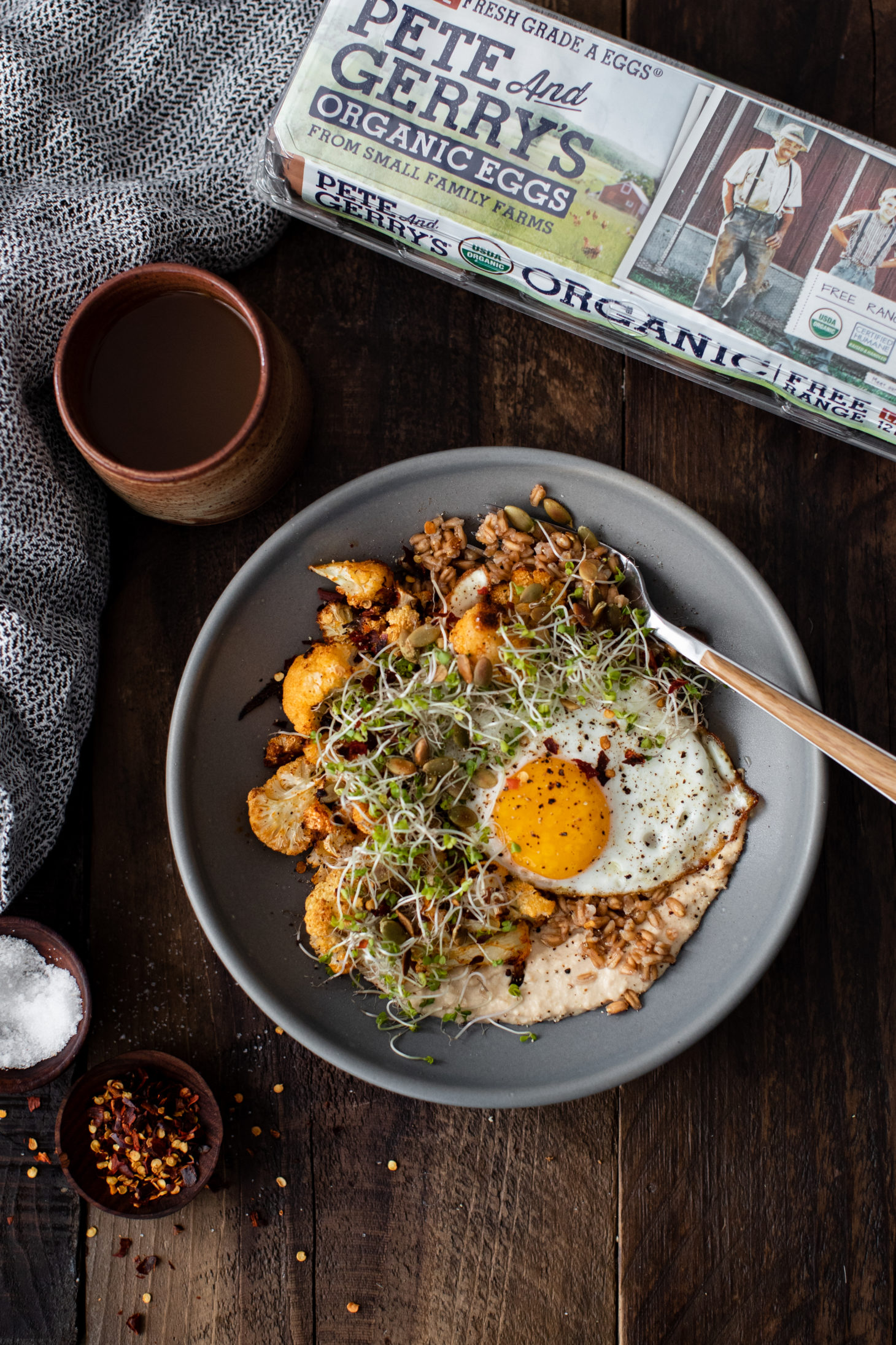 Overhead photograph of a cup of coffee and grey bowl with grains and a fried egg.