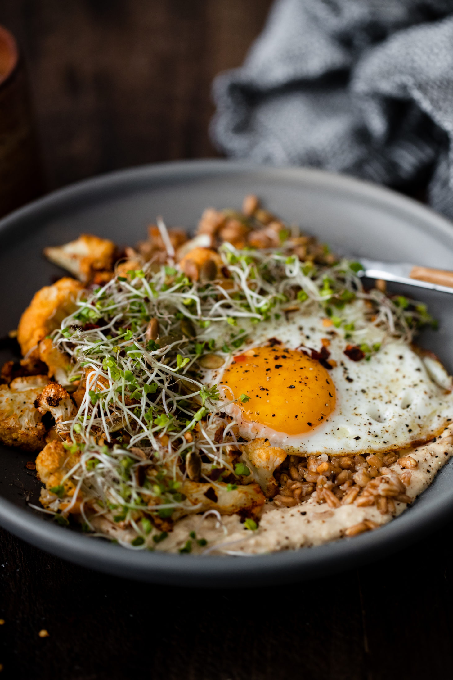 Side-angle photograph of a fried egg on-top of farro, hummus, and smoked paprika roasted cauliflower.