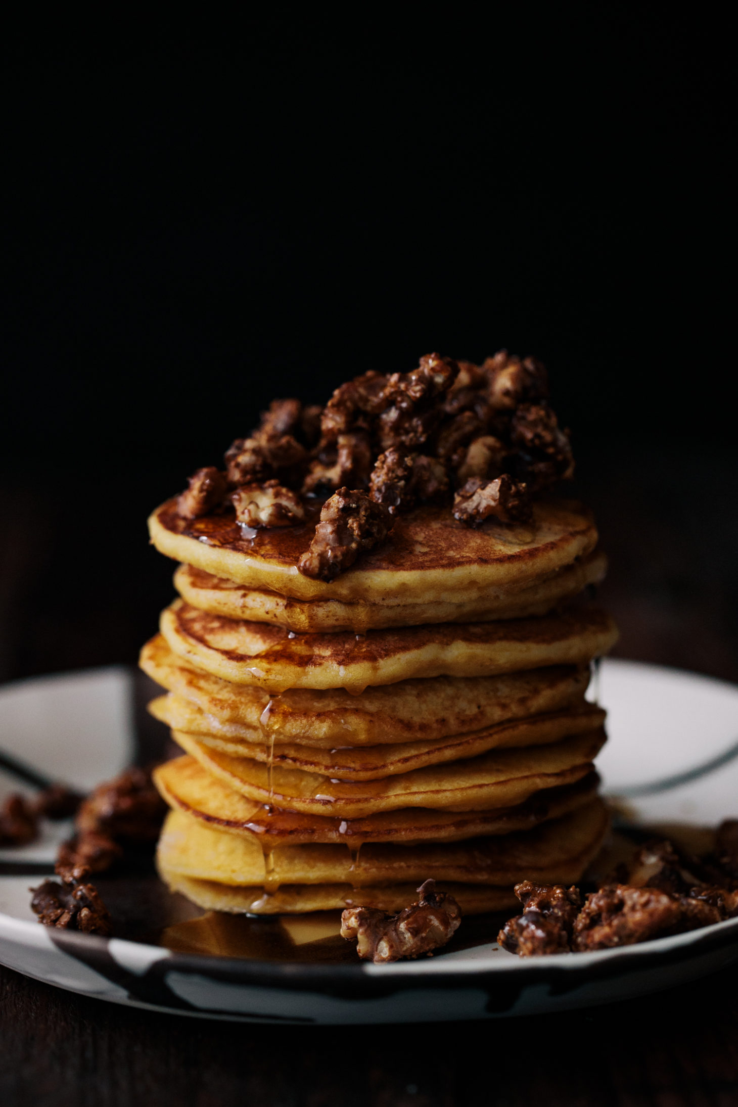 Photograph of ricotta pancakes from the side, topped with candied walnuts and maple syrup.