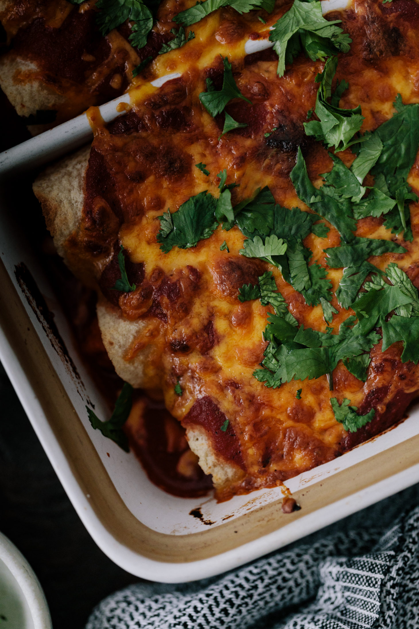 Close-up photograph of sweet potato enchiladas with spiced pinto beans and topped with melted cheddar cheese and cilantro. 