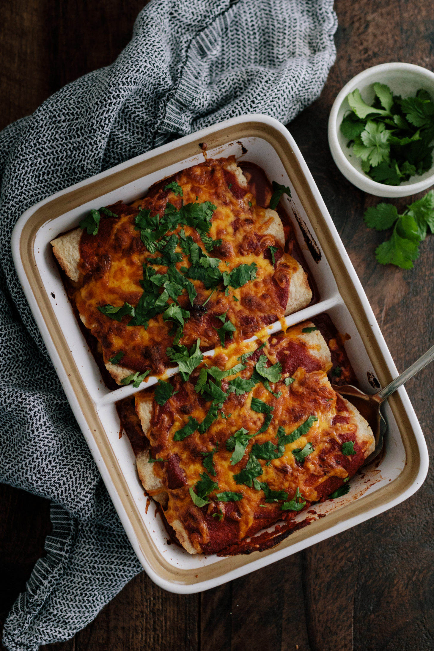 Close-up photograph of sweet potato enchiladas with spiced pinto beans and topped with melted cheddar cheese and cilantro. 