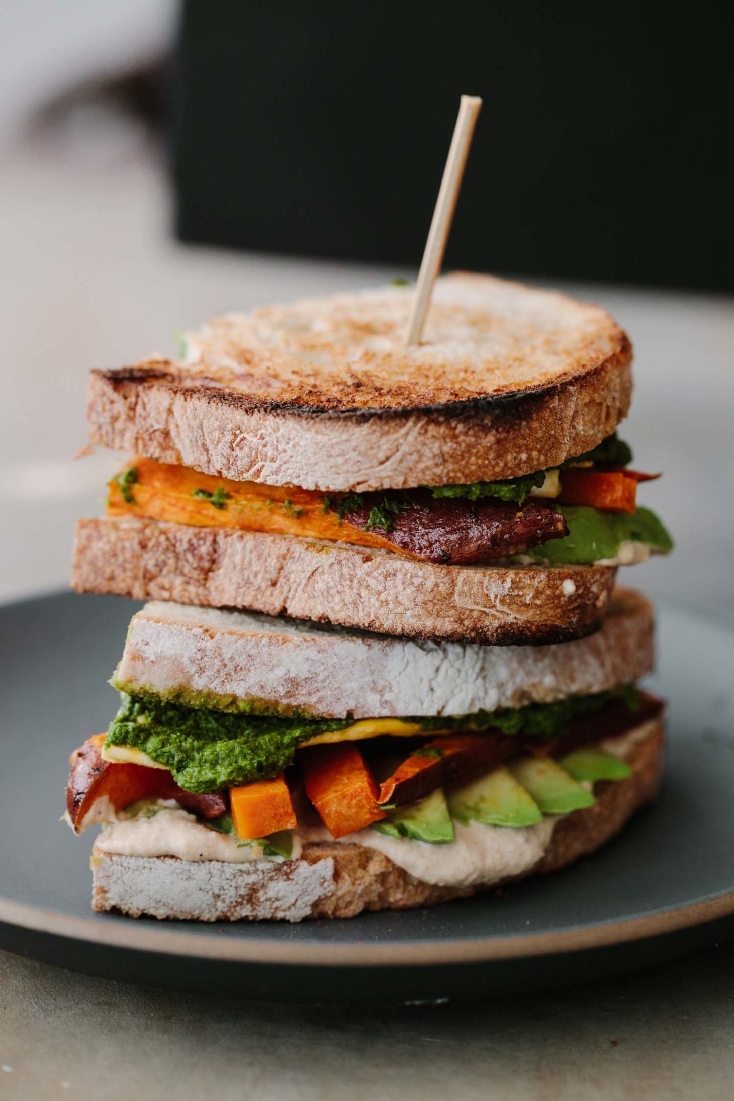 Side-angle photograph of sandwich cut in half and stacked on top of each other with hummus, sweet potato, avocado, and eggs.