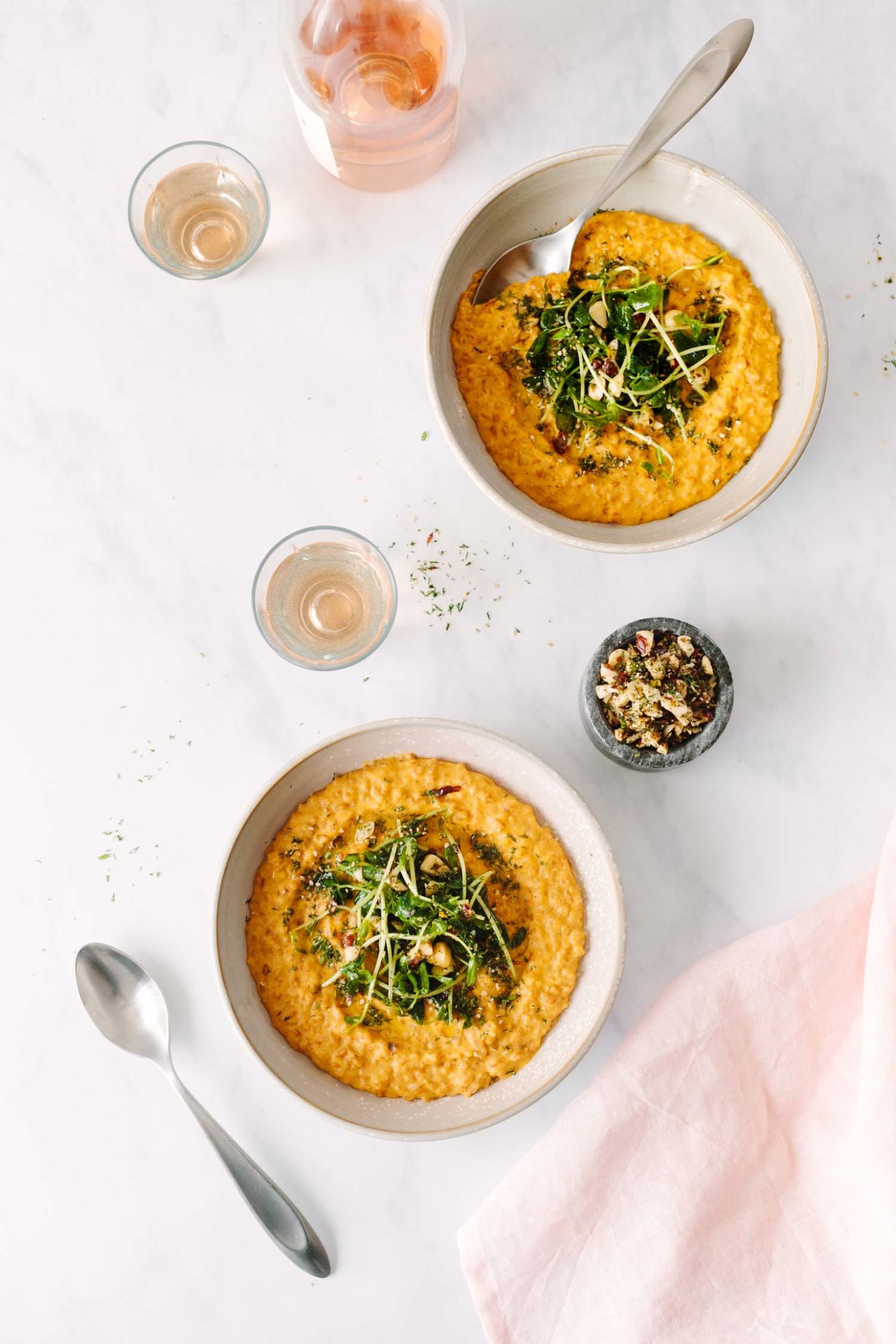 Overhead photograph of two bowls of Creamy Vegan Carrot Risotto Topped with Pea Shoots and Dill Hazelnuts.