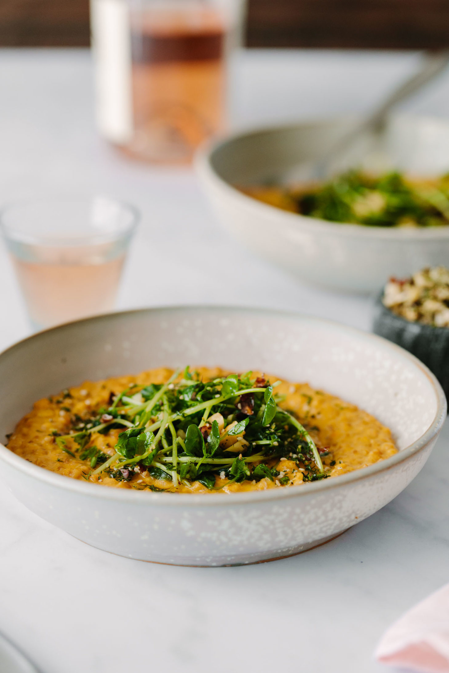 Side-angle of Vegan Carrot Risotto Topped with Pea Shoots and Dill Hazelnuts.