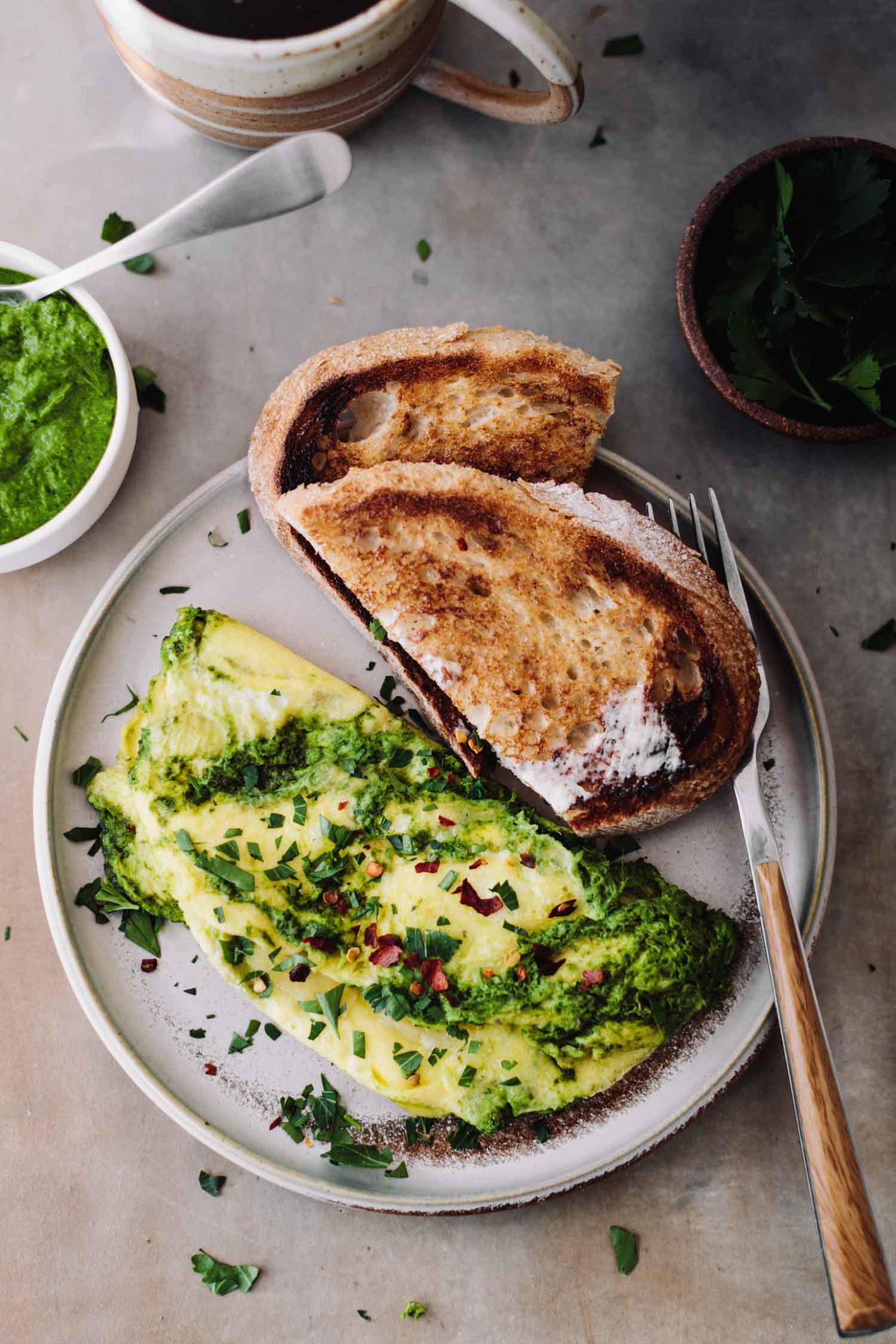 Overhead photo of Omelette with a tarragon-kale sauce and melted manchego served with extra sauce and coffee.