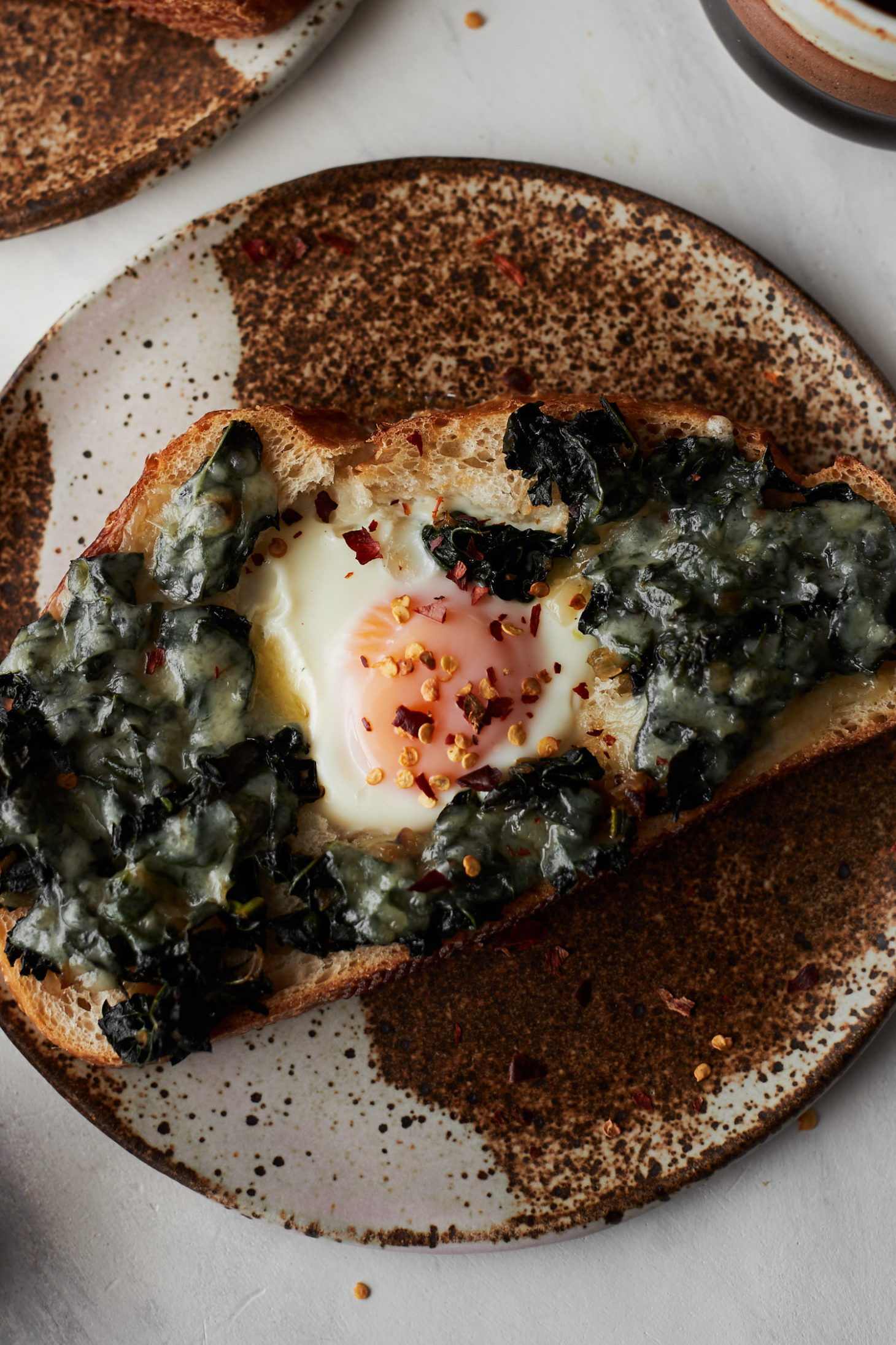 Overhead photograph of two pieces of toast with egg in a hole, sautéed kale, and melted cheese.