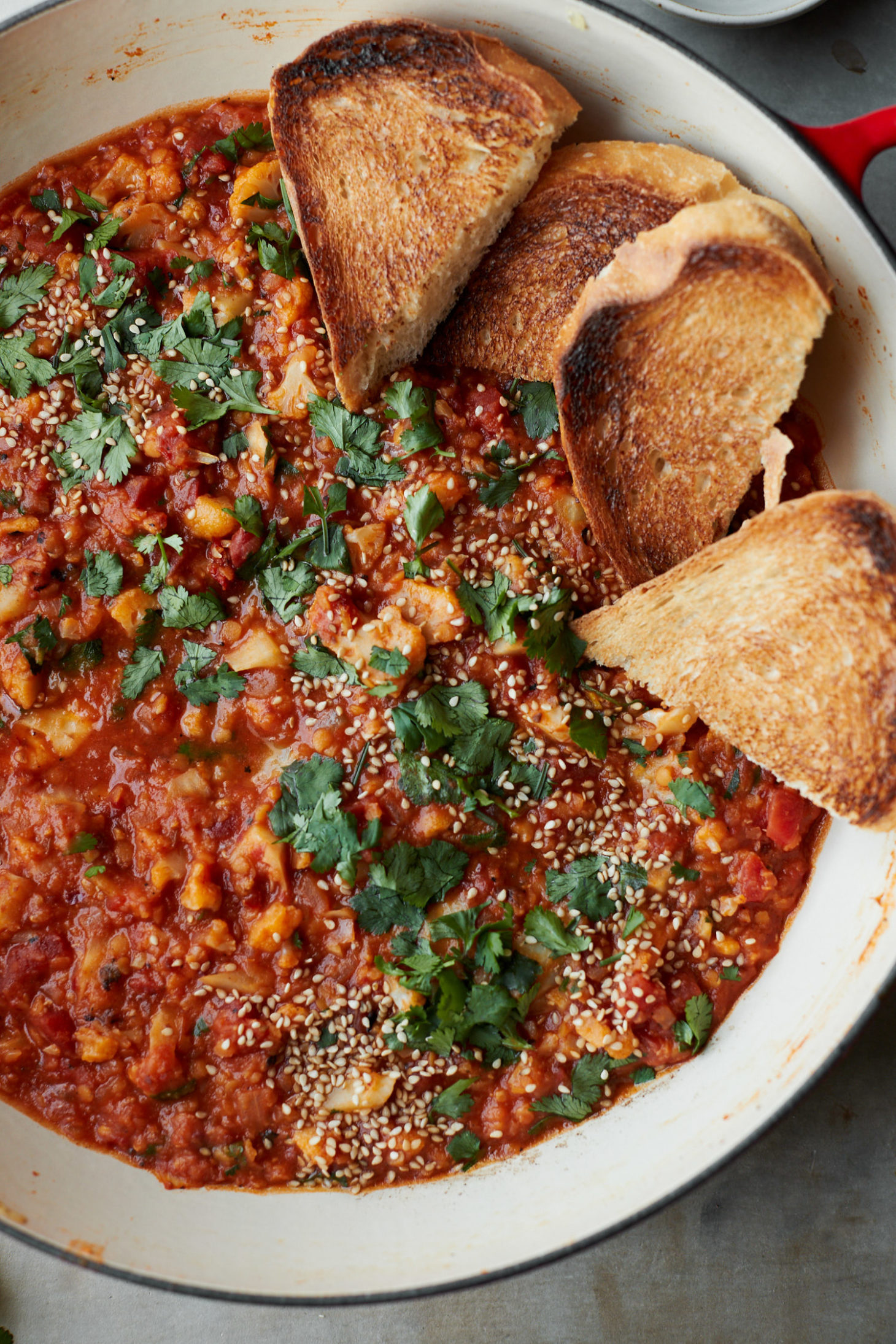 Close-up photograph of an overhead white dutch oven with red lentils, tomato sauce, and cauliflower. 