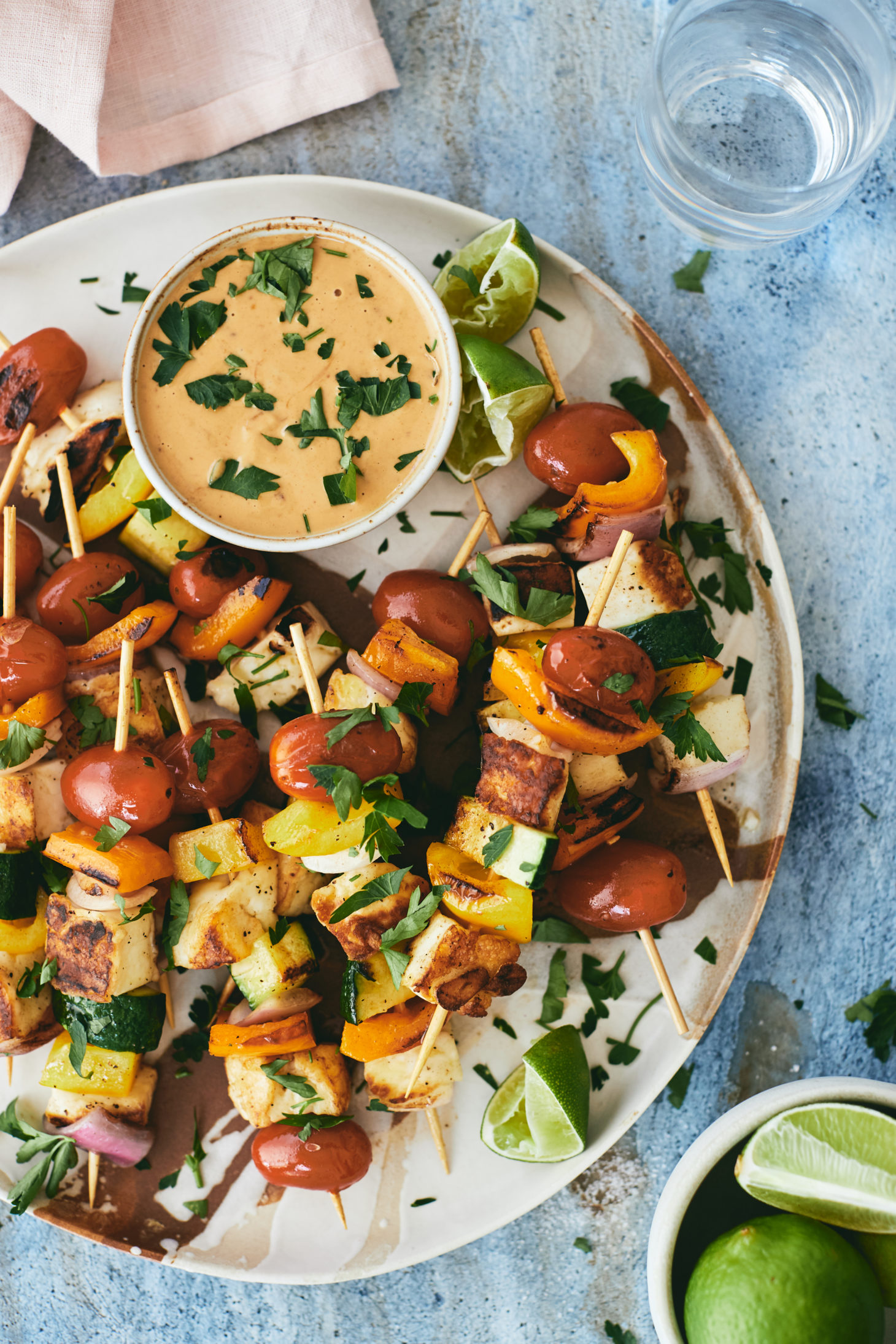Close-up overhead photograph of halloumi skewers with summer vegetables and a peanut sauce on the side.