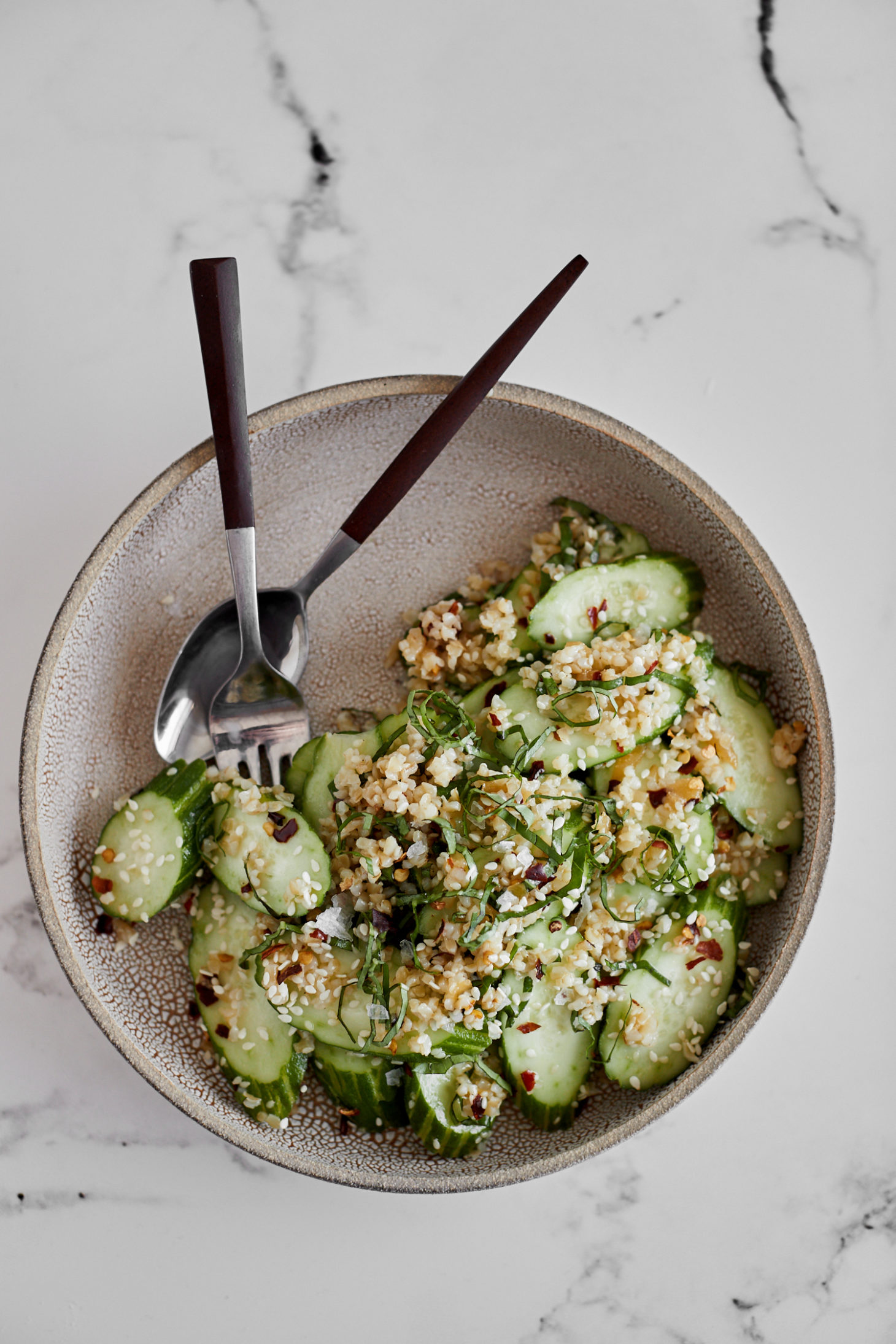 Overhead photo of a tan bowl on marble background with a cucumber salad. 