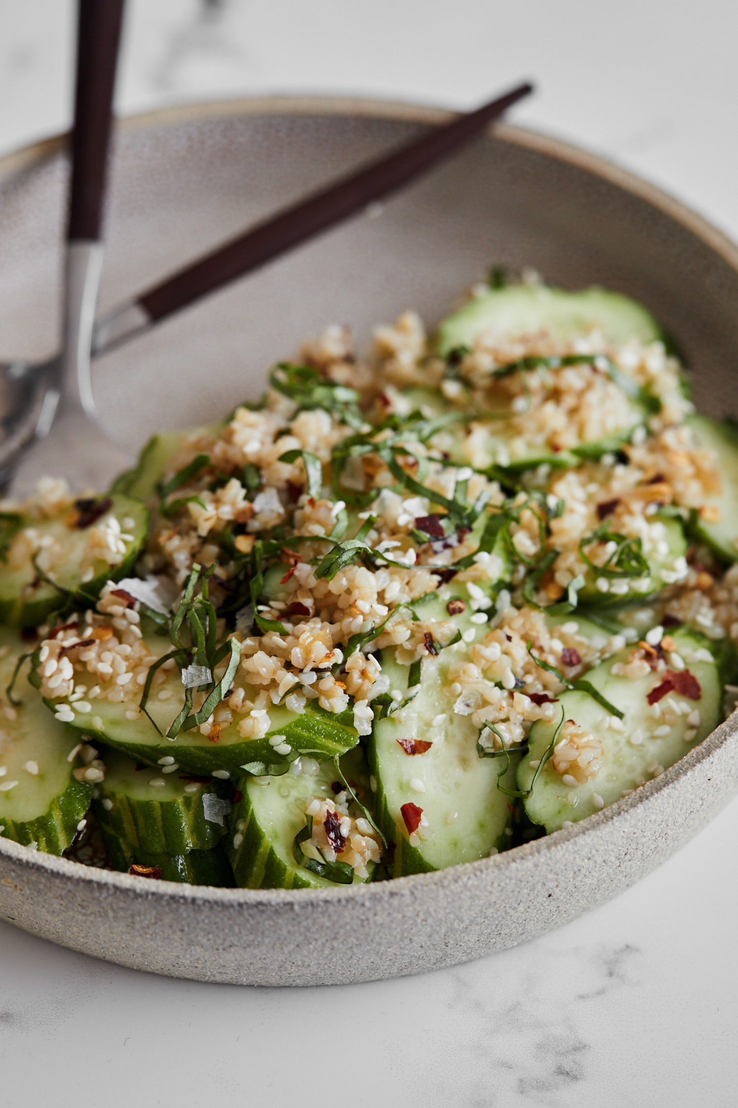 Close-up, side angle photograph of a cucumber salad tossed with bulgur and sesame seeds.
