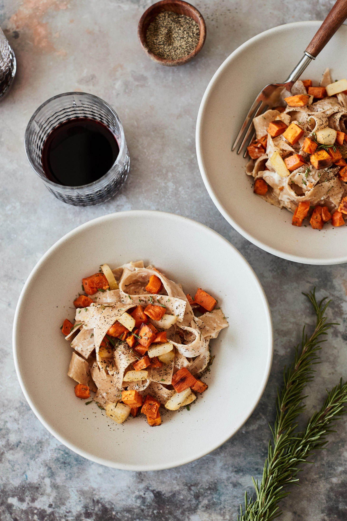 Image of two bowls of pasta with roasted orange sweet potato and a glass of red wine.