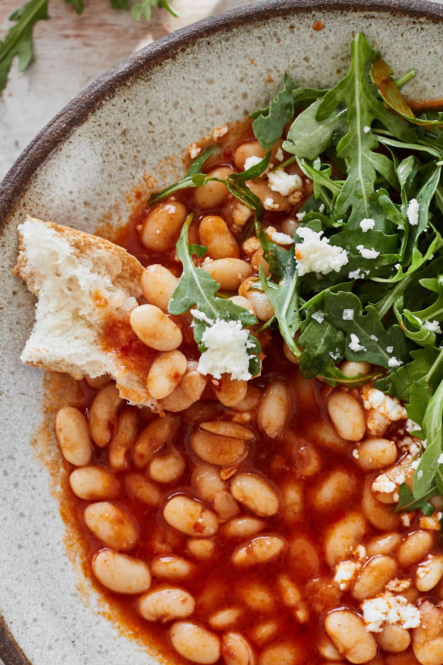 Close-up image of a piece of bread topped with beans in a red broth.