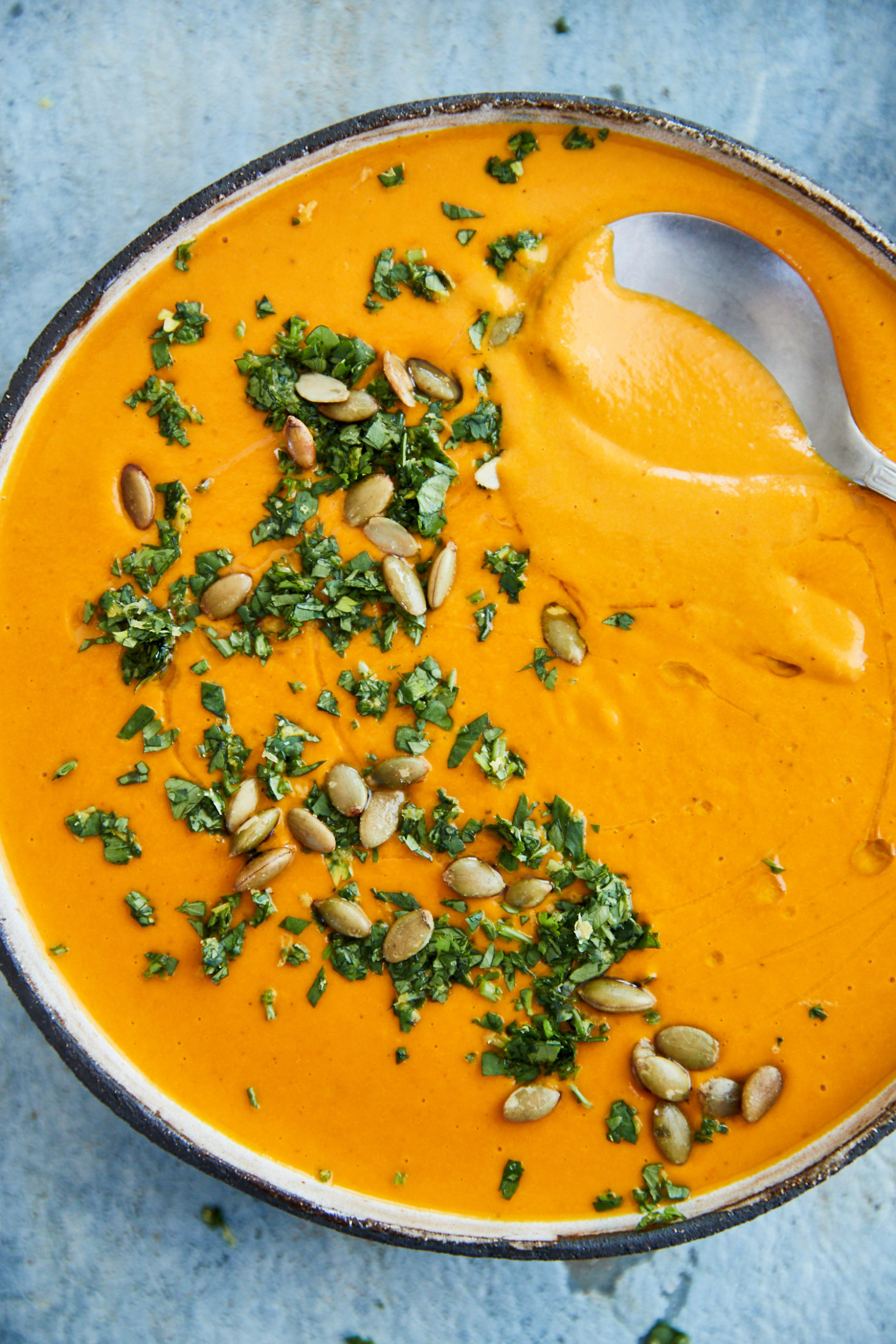 close-up photo of a silver spoon in a bowl of orange carrot soup.
