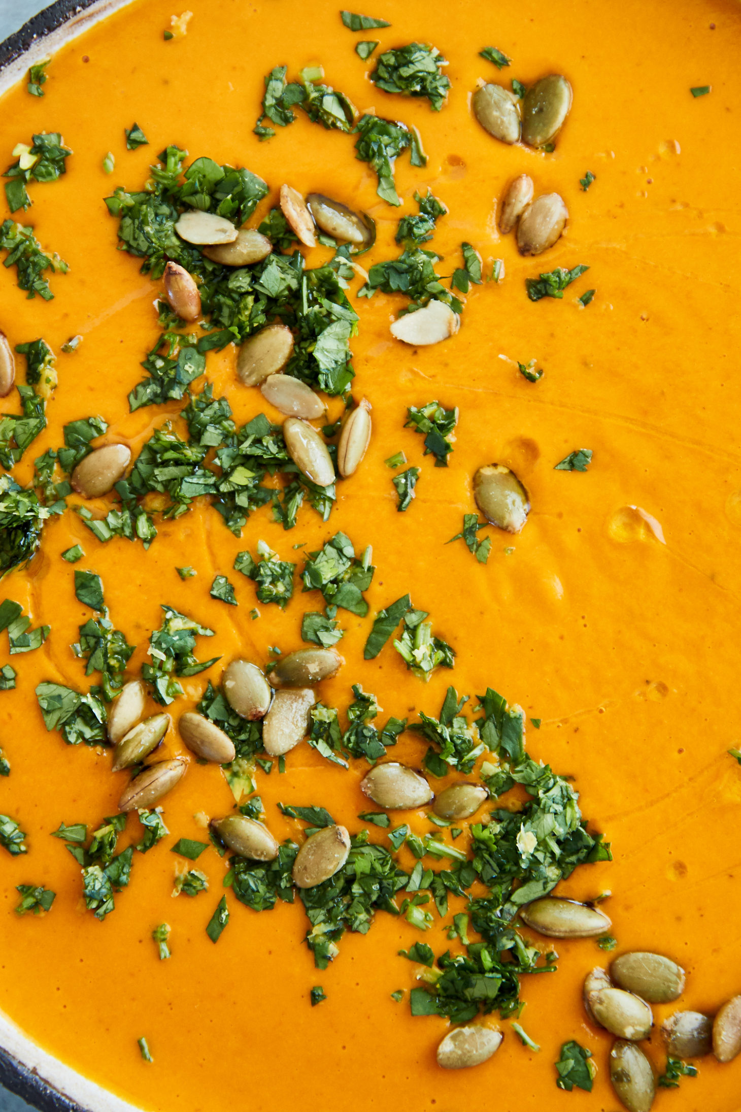 Close-up photo of orange carrot soup topped with cilantro and green pepitas.