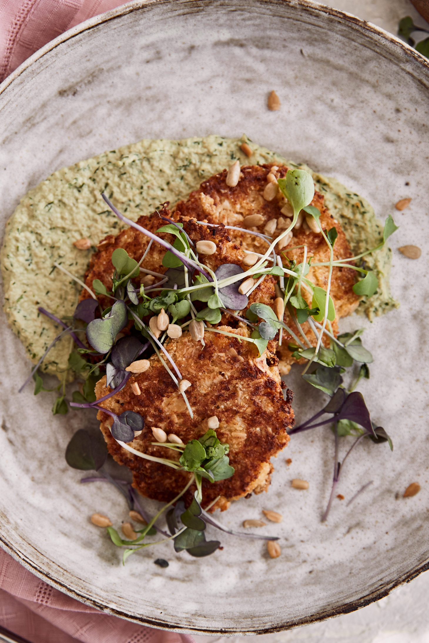 Close-up image of pan-fried cauliflower fritters in a larger white bowl. 