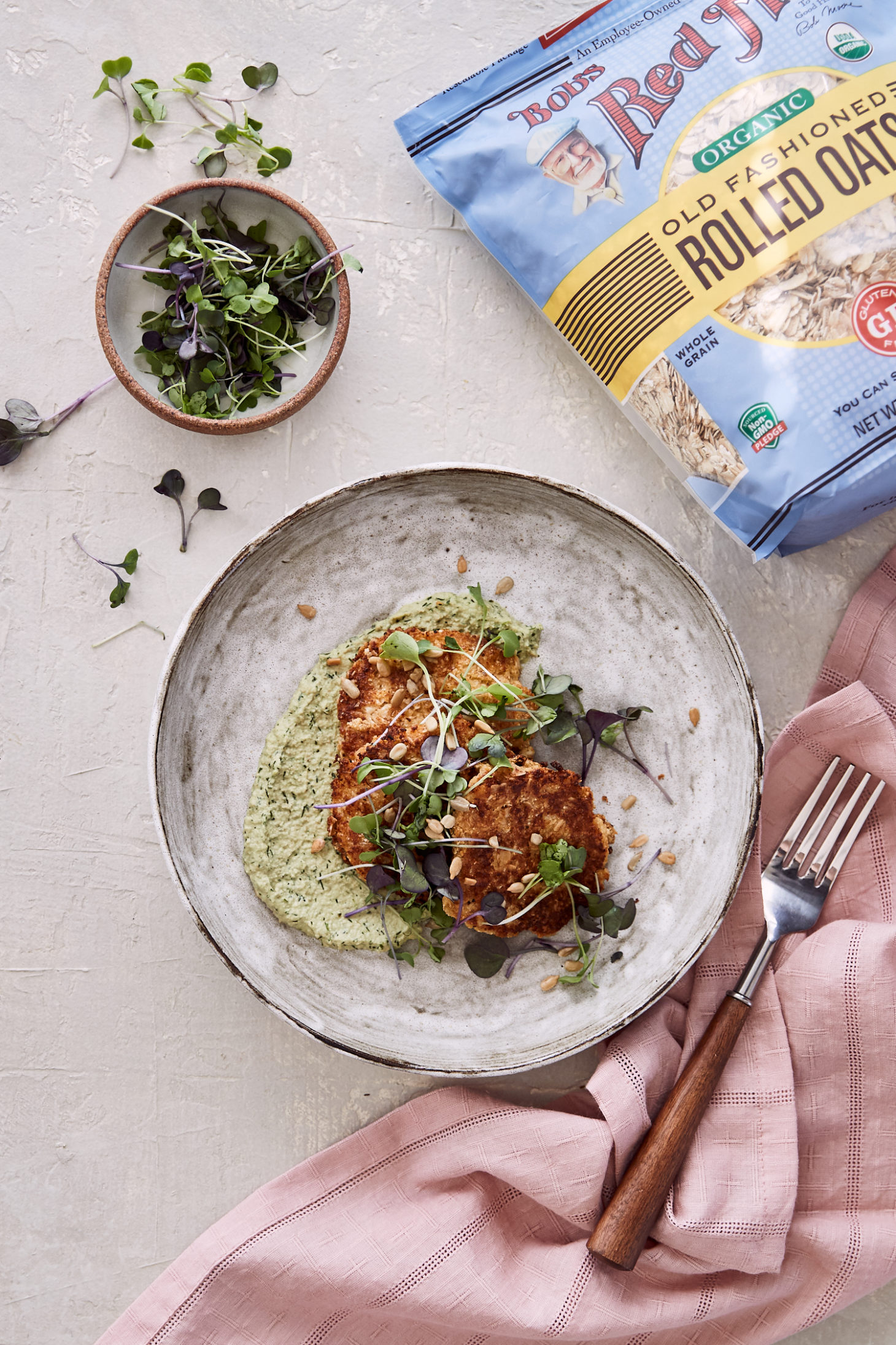 Image of a large white bowl on a grey background with cauliflower fritters, herb spread. 