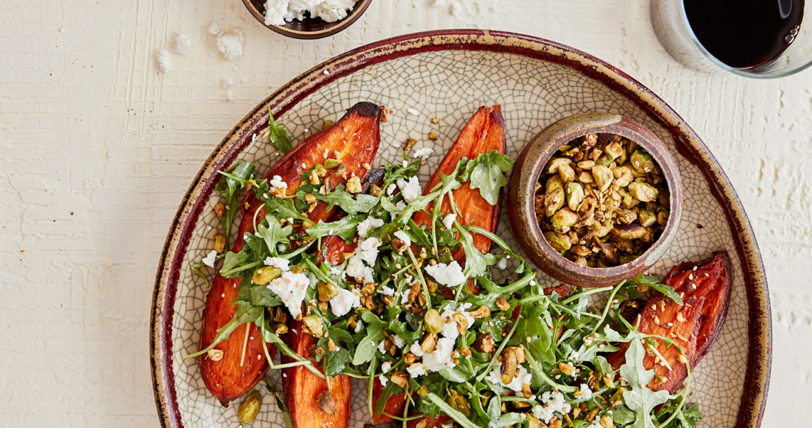 overhead image of sweet potatoes covered with arugula on a crackled large plate