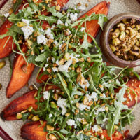 a light crackled plate with sweet potatoes topped with arugula and pistachios