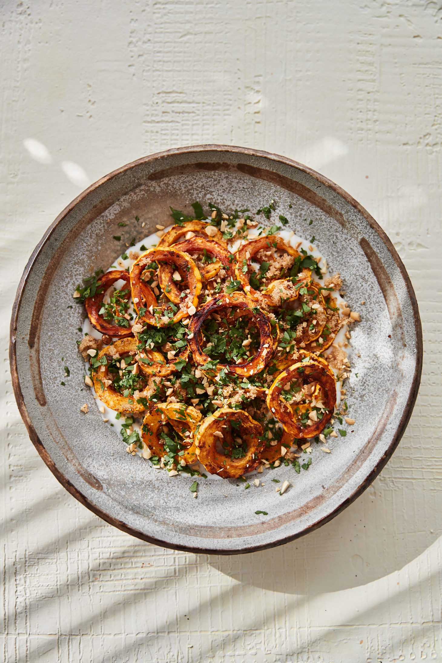 Photograph of a low grey bowl filled with roasted delicata squash and yogurt on a cream textured surface.