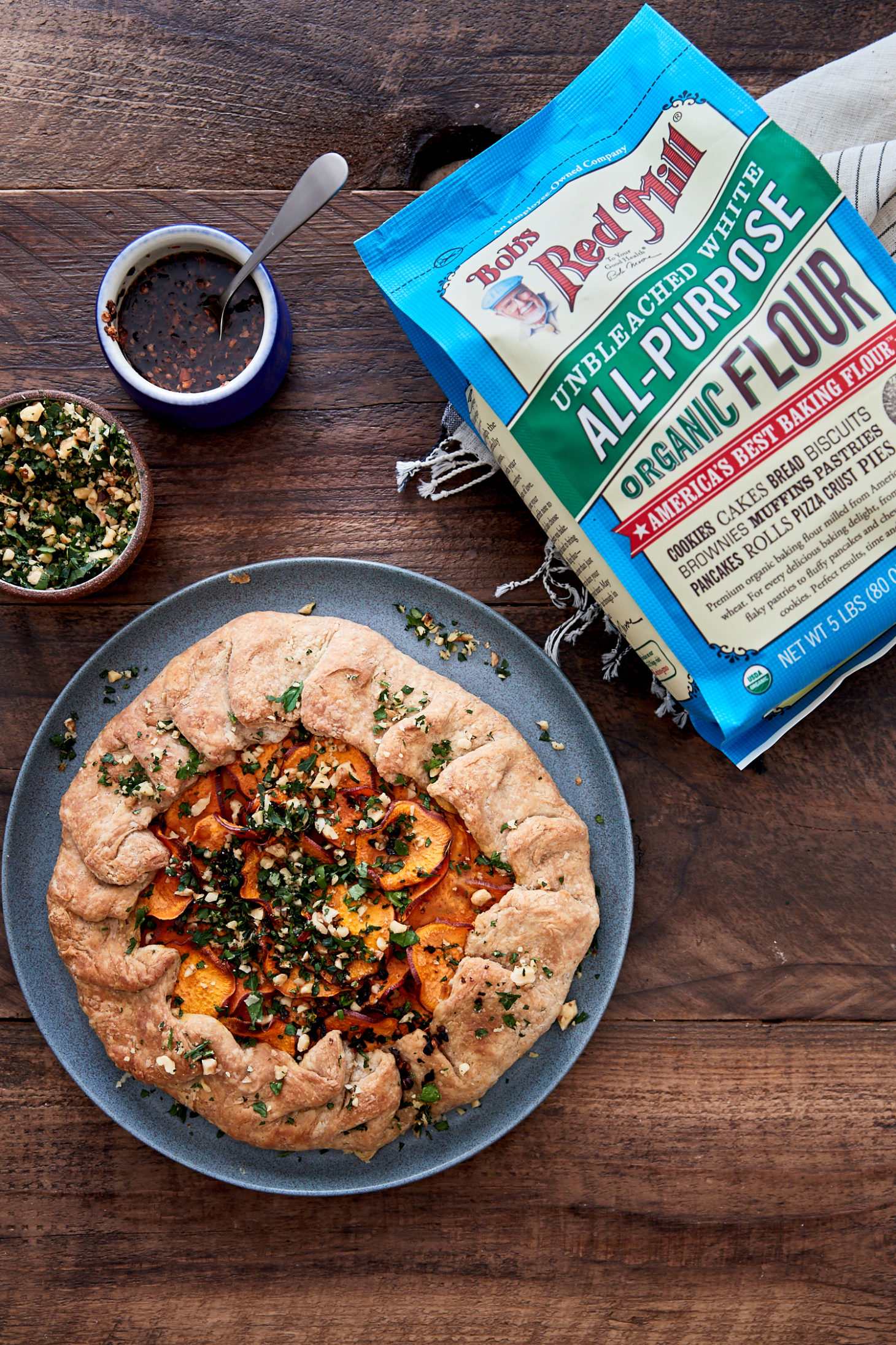 Image of a sweet potato galette on blue plate with chili oil and a bag of Bob's Red Mill All Purpose Flour