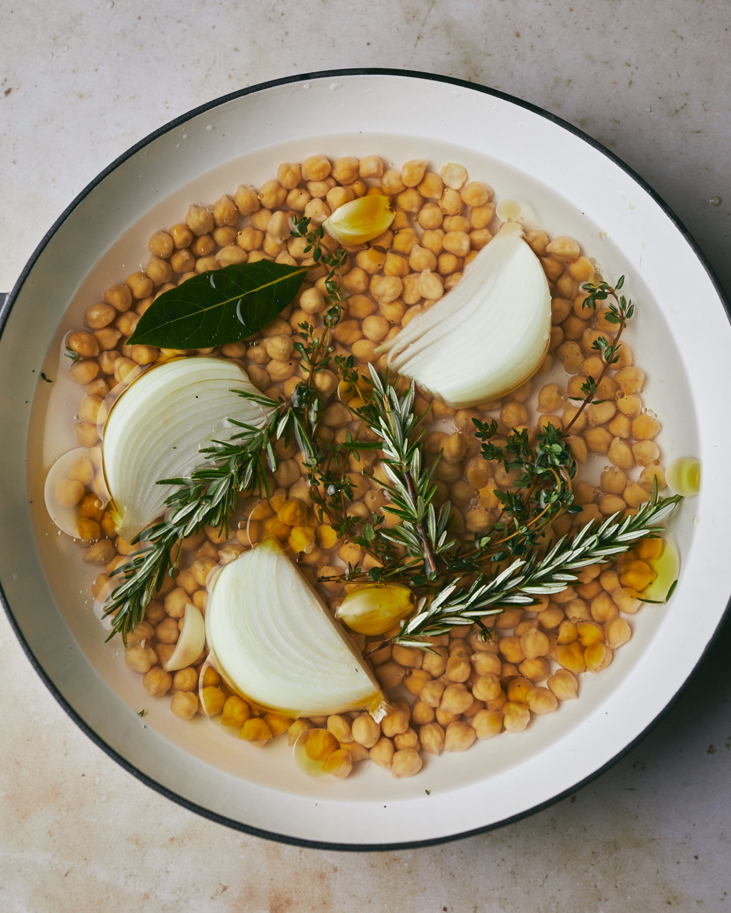 Close-up photo of soaked beans in a pot with herbs, onions, garlic, and olive oil